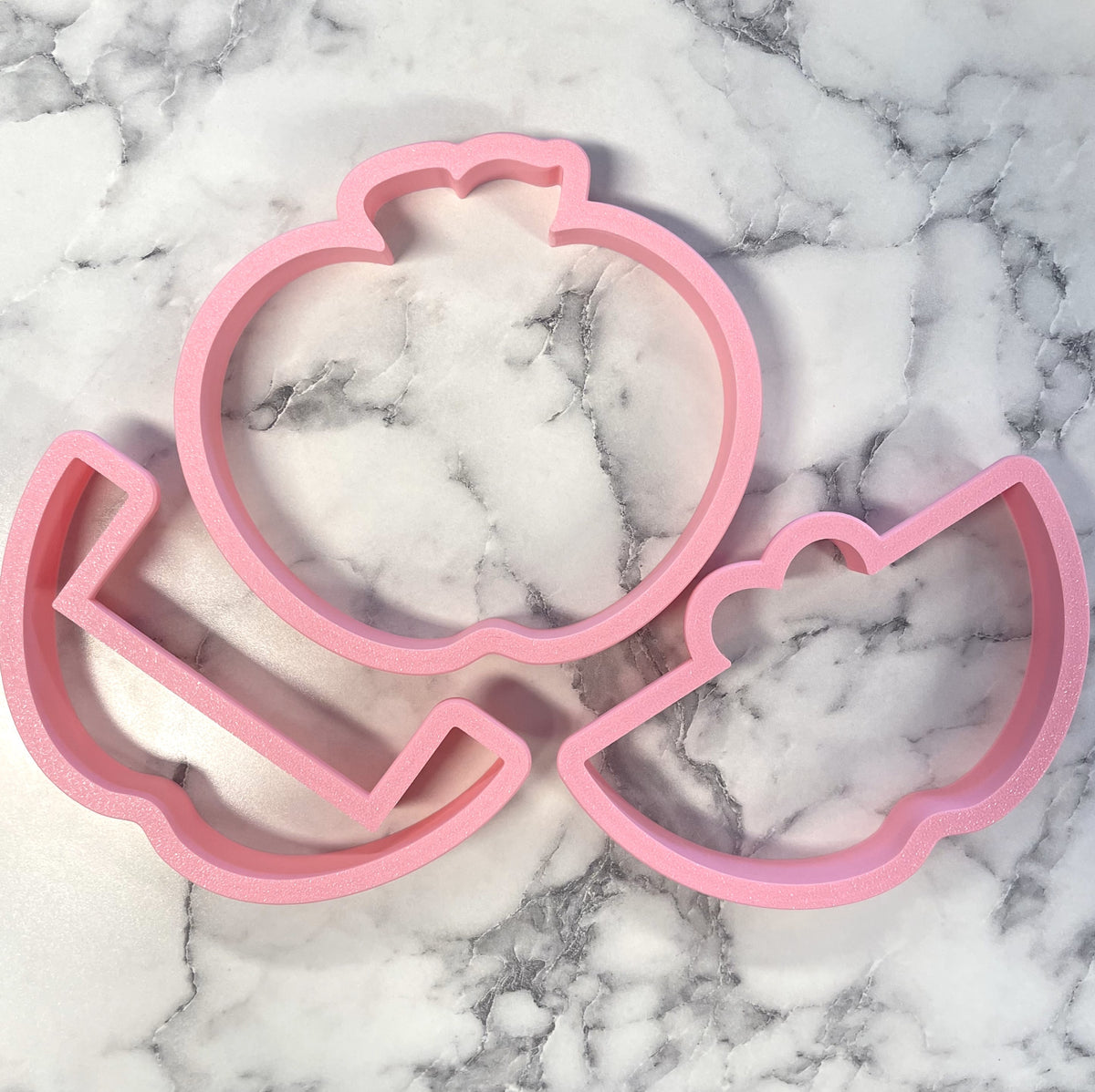 Pink silicone cookie cutter shaped like a cartoon pumpkin with a smiling face and curly hair from a 3pc apple gift card holder set