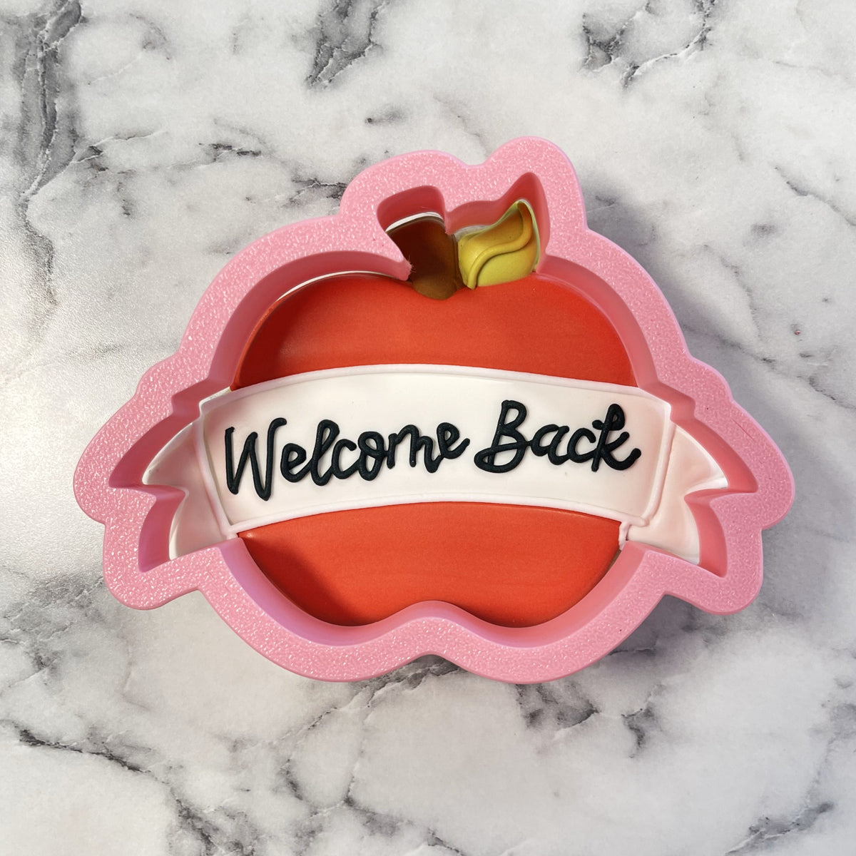 Pink glitter apple banner plaque cookie cutter with white ribbon banner reading welcome back in black cursive