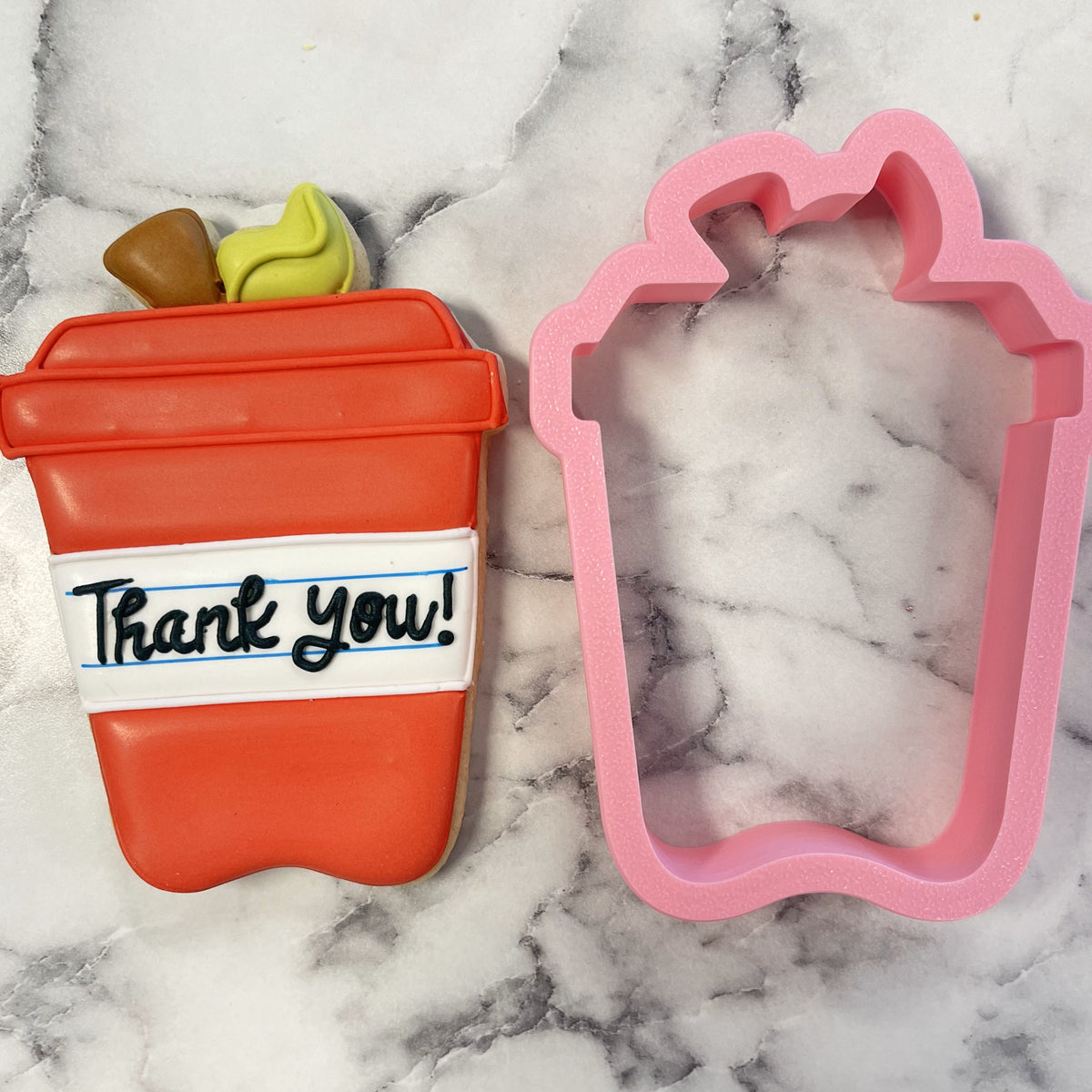 A vibrant orange apple latte cookie shaped like a coffee cup with a thank you message and a pink silicone cutter
