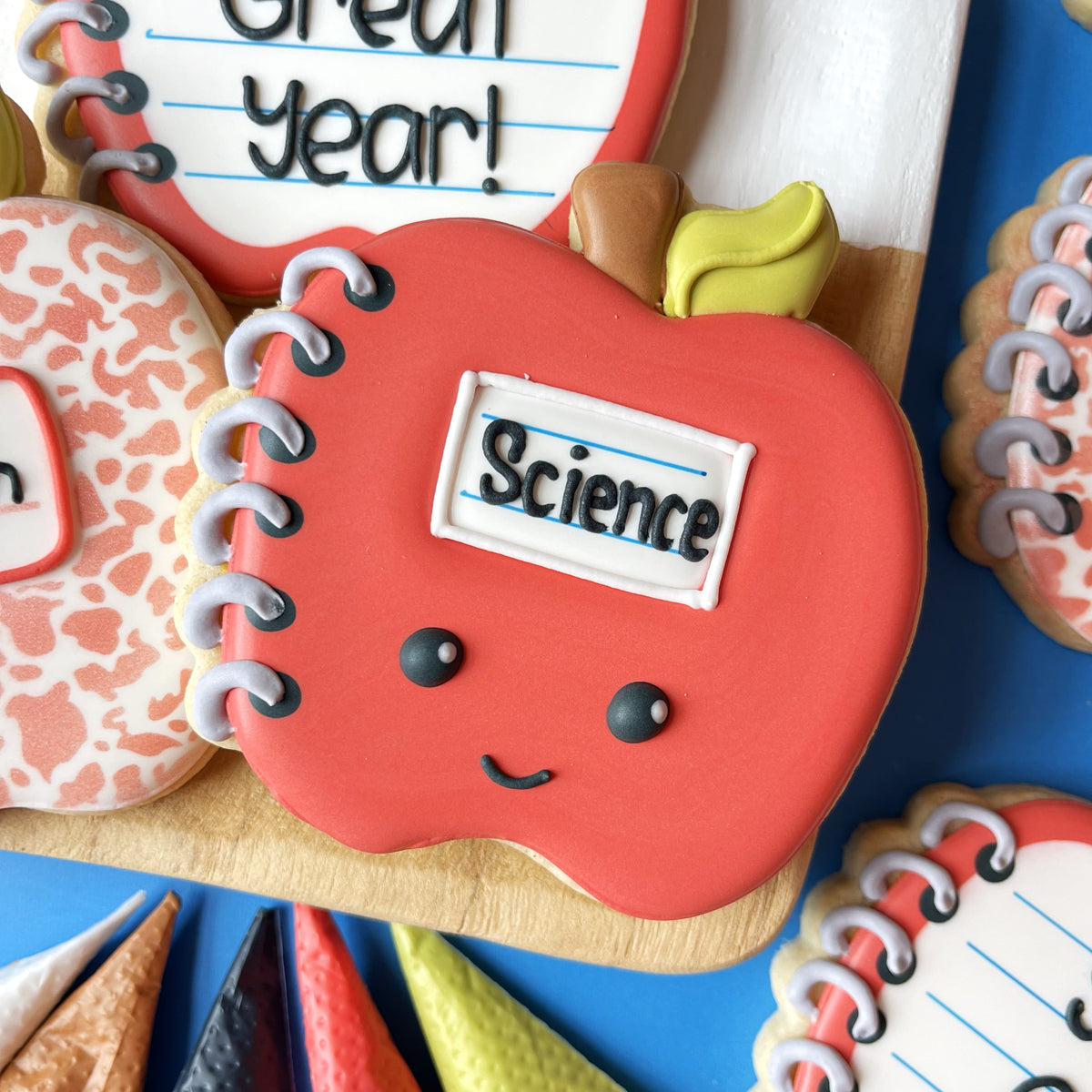 A red smiling notebook-shaped cookie with science label and silver icing spiral made with apple notebook cookie cutter