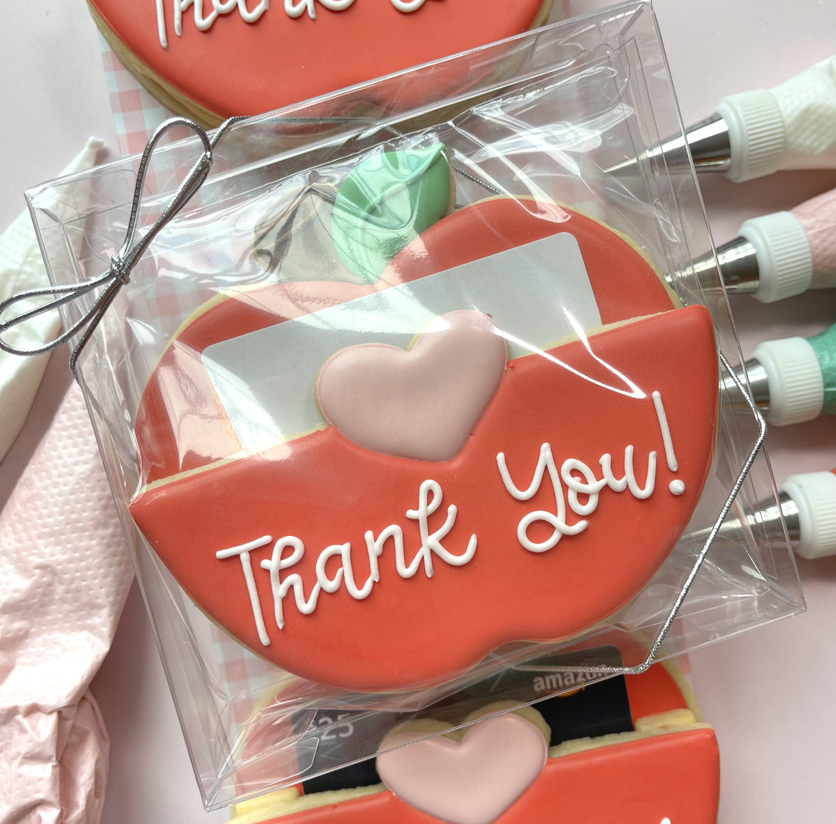 Red apple-shaped cookie with white thank you icing and pink heart in clear cellophane from 3pc apple gift card cutter set