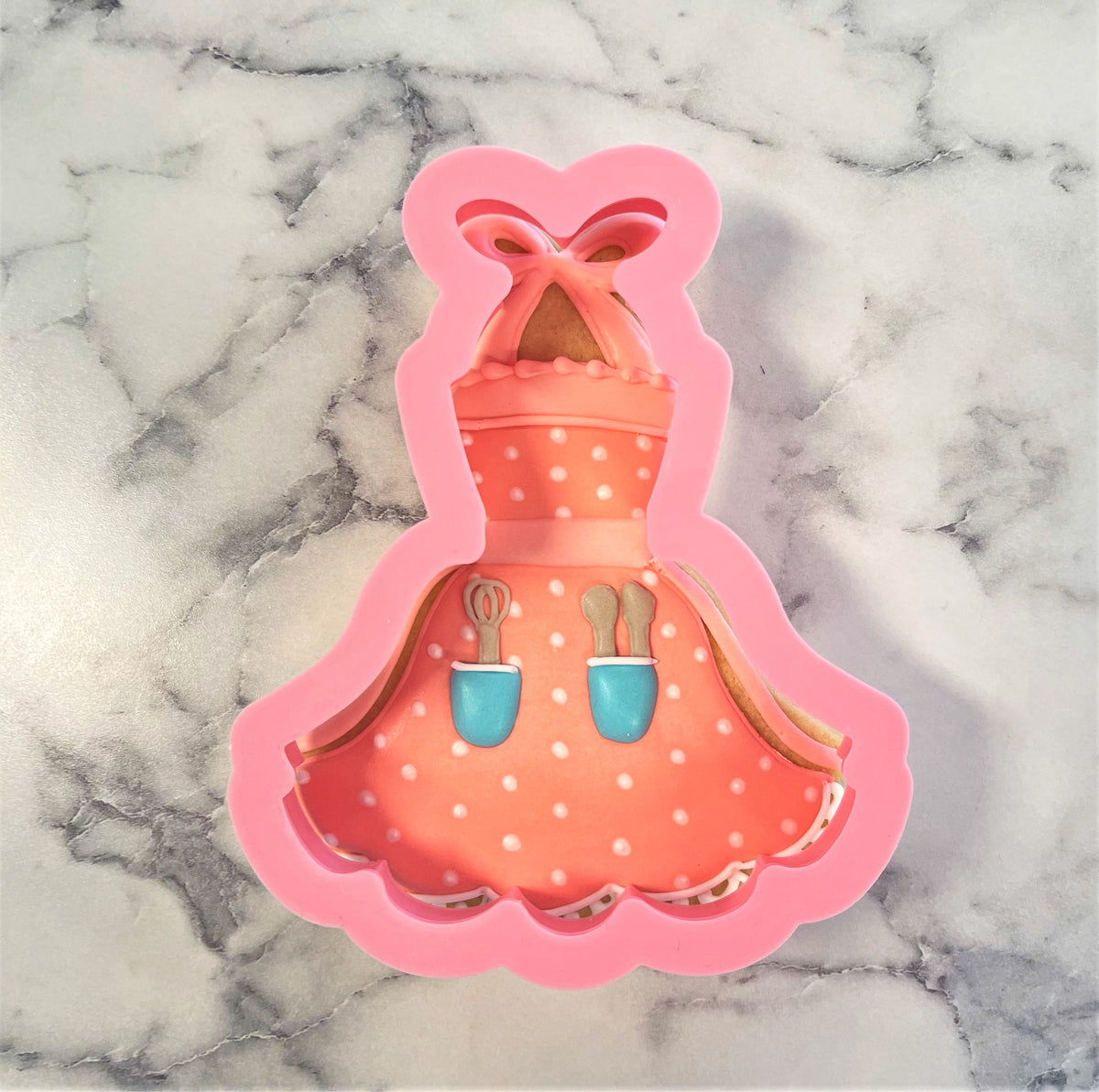 Pink silicone apron tutu cookie cutter with polka dots and attached utensils for baking and decorating