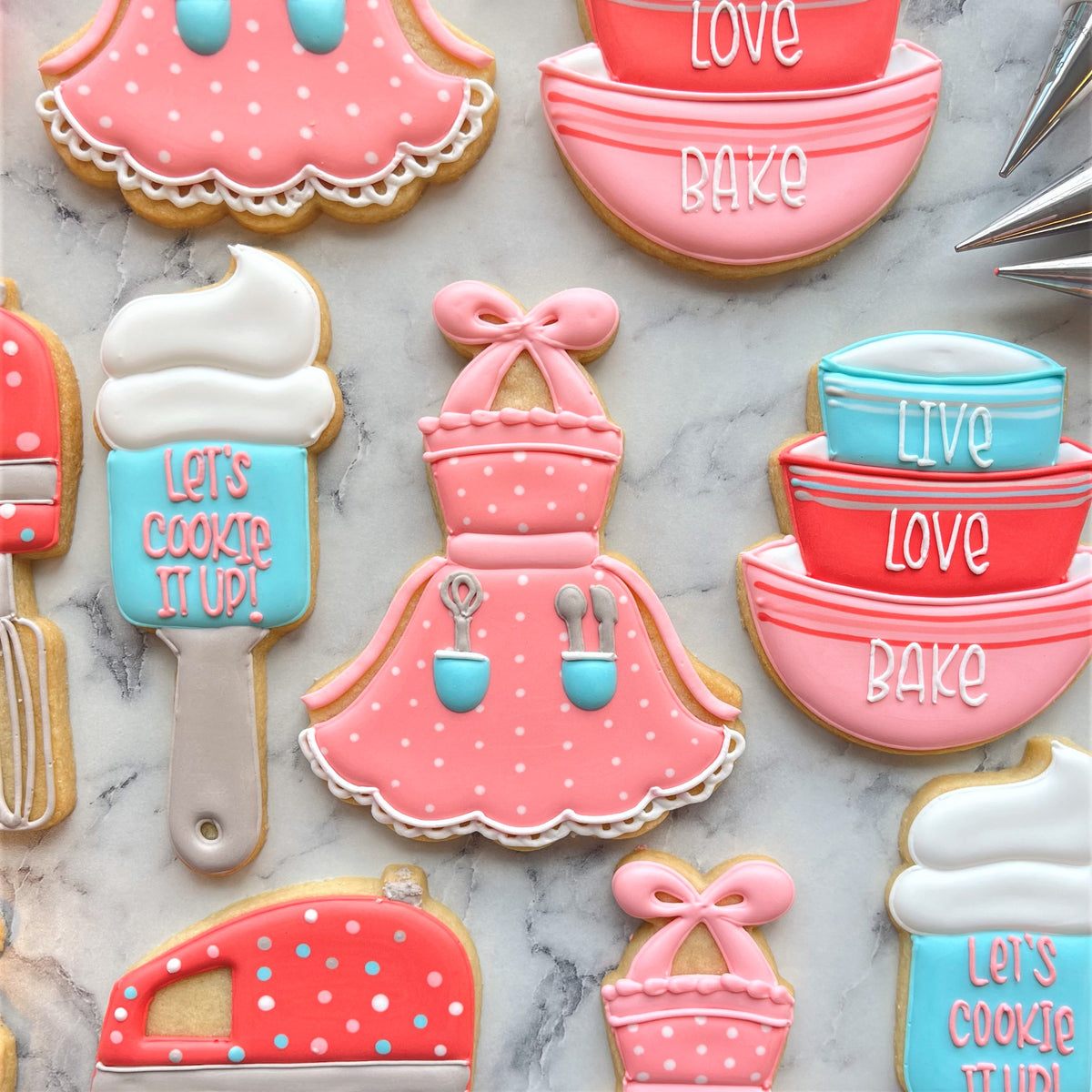 Pink polka-dot apron-shaped cookie with white lace trim and blue utensil details made using apron tutu cookie cutter
