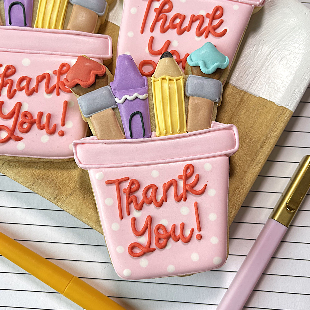 Pink polka-dotted art cup cookie cutter shaped like pencil case filled with colorful icing crayons and pencils