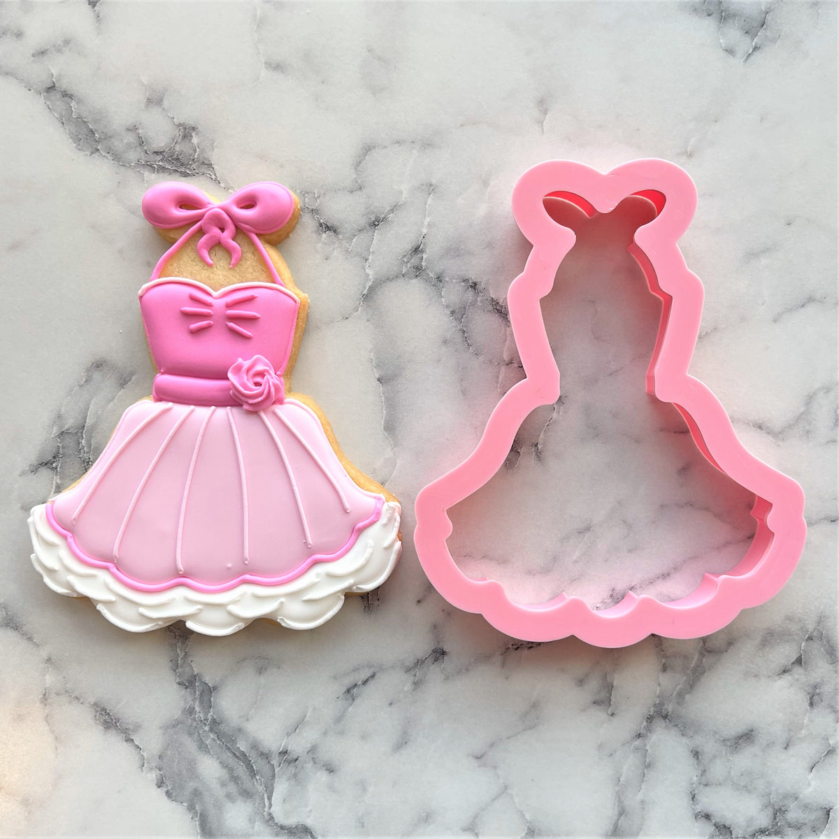 Pink silicone apron tutu cookie cutter next to decorated pink and white sugar cookie for baking use