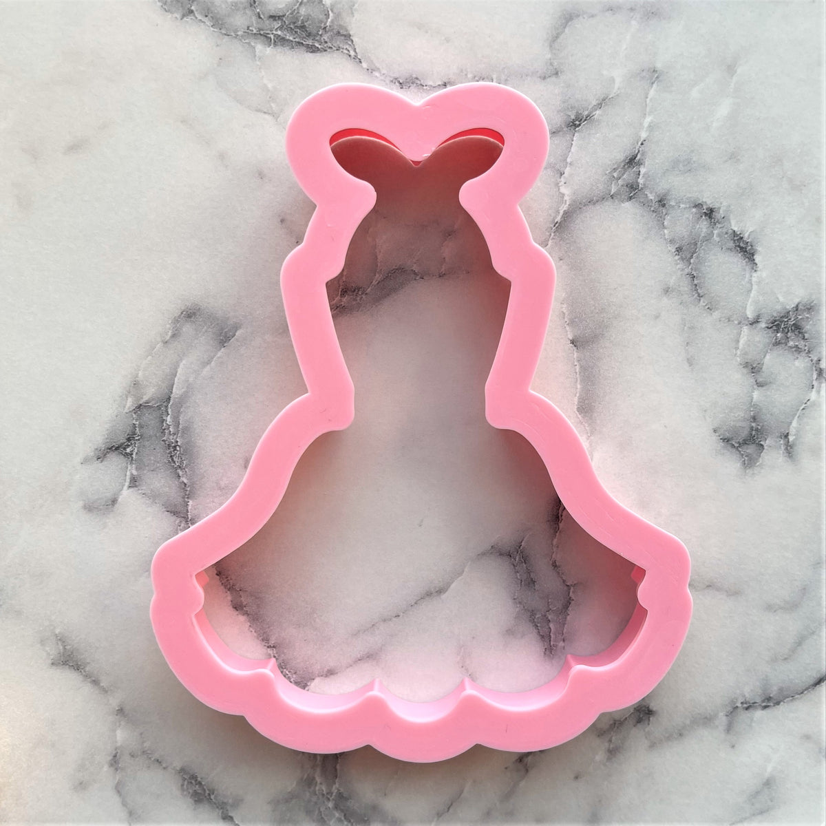 Pink plastic apron tutu cookie cutter shaped like a princess dress with heart neckline and scalloped hem