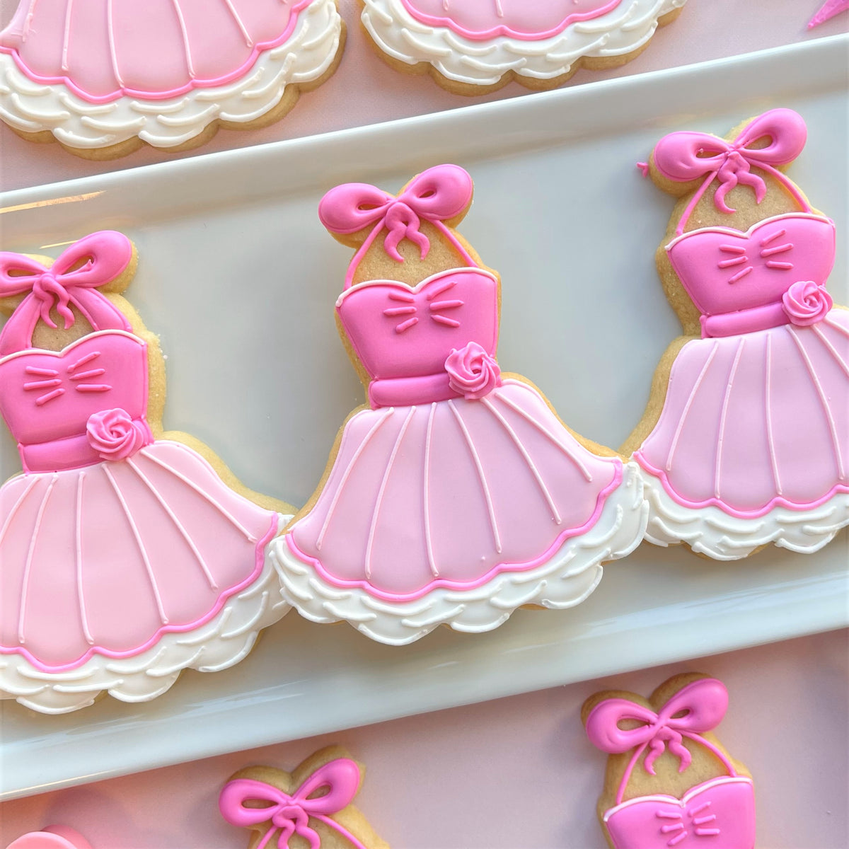 Pink iced dress-shaped apron tutu cookies with white lace trim and pink bows made using a cookie cutter