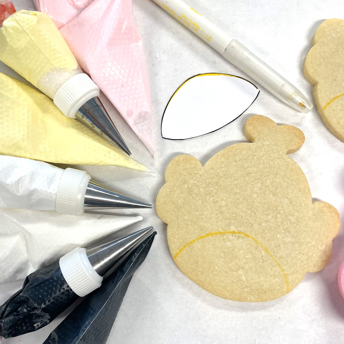 Squishie bee cookie cutter with unpainted light brown bear-shaped sugar cookie outlined in yellow icing