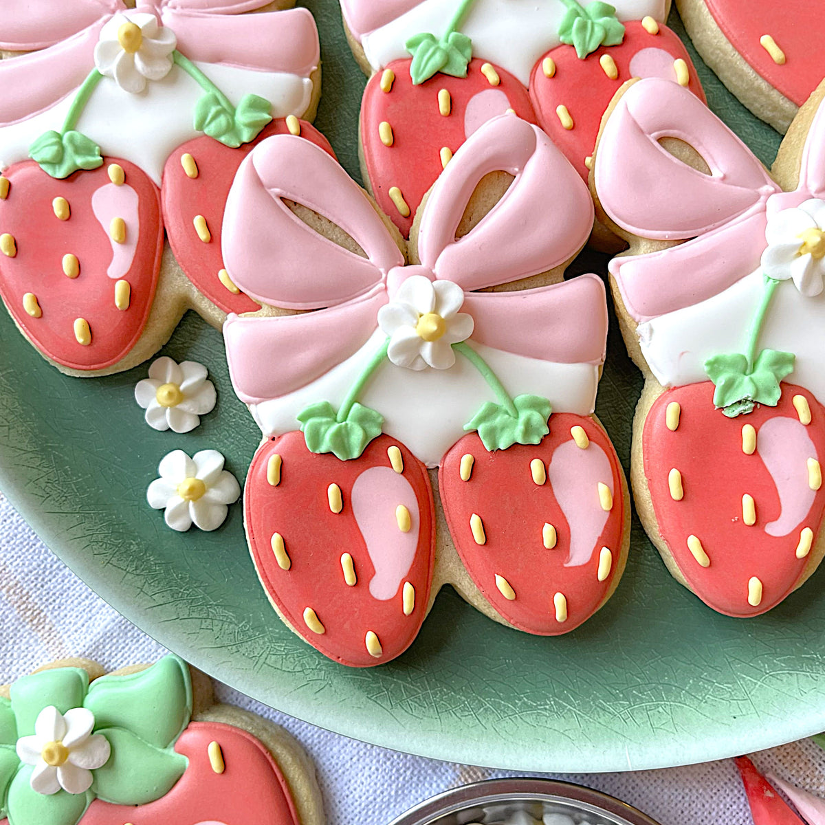 Pink-frosted strawberry-shaped cookies with yellow icing seeds and white floral decorations made with berries with bow cookie cutter