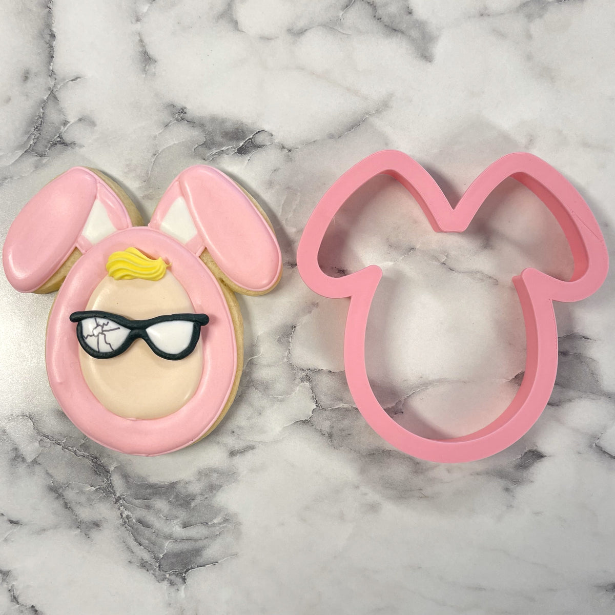 Pink bunny costume cookie cutter with black-framed glasses and yellow hair detail on decorated cookie