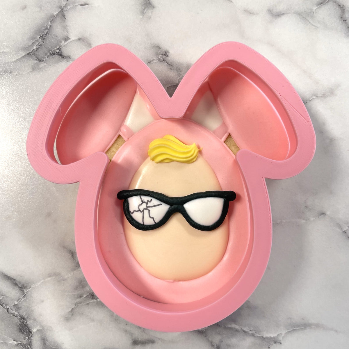 Pink bunny costume cookie cutter with molded face featuring blonde hair and black framed glasses for baking use
