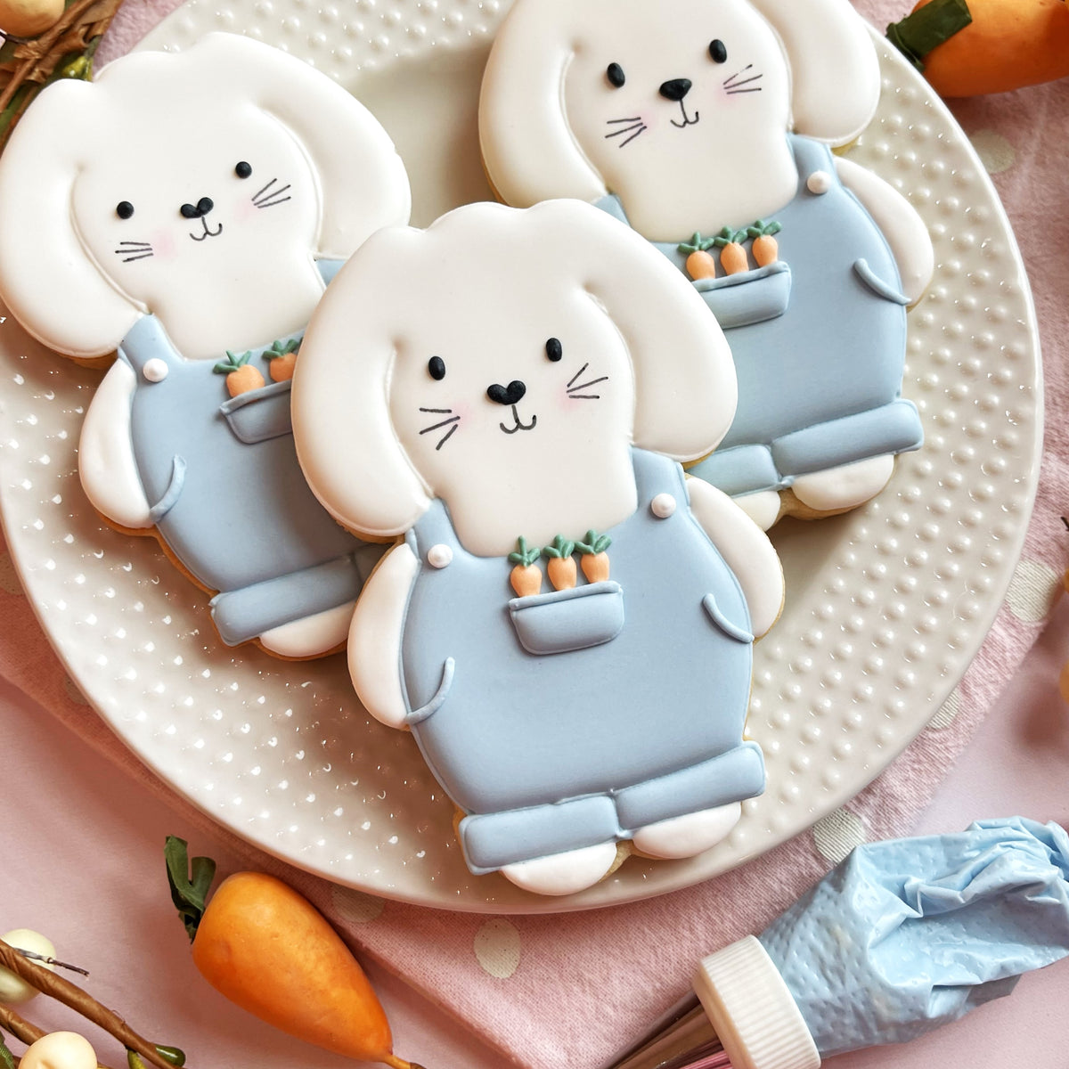 Delicate white bunny-shaped cookies with light blue overalls and orange carrot decorations from bunny farmer cookie cutter bundle with stencil