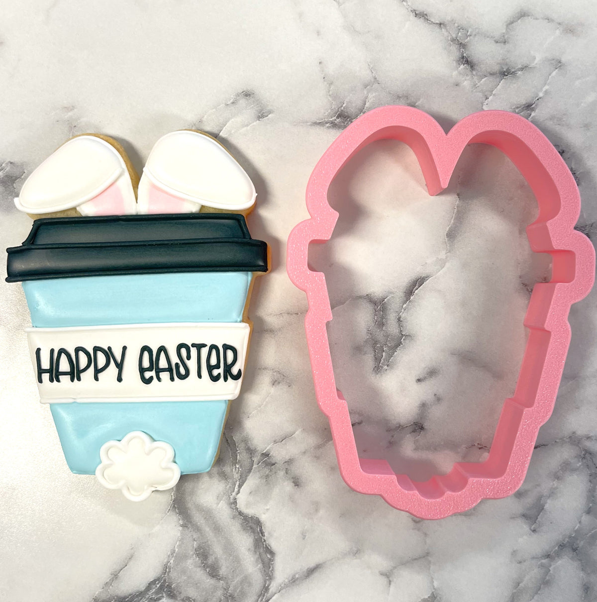 A pastel blue bunny latte cookie shaped like a coffee cup with bunny ears and happy easter text on top