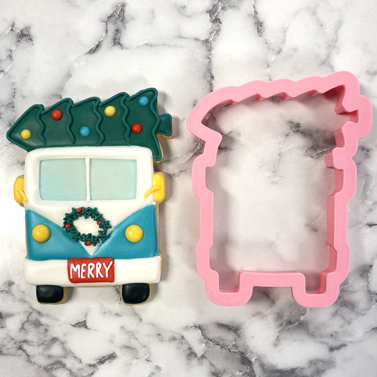 A festive cookie shaped like a vintage van with a christmas tree on the roof decorated in white teal and yellow icing