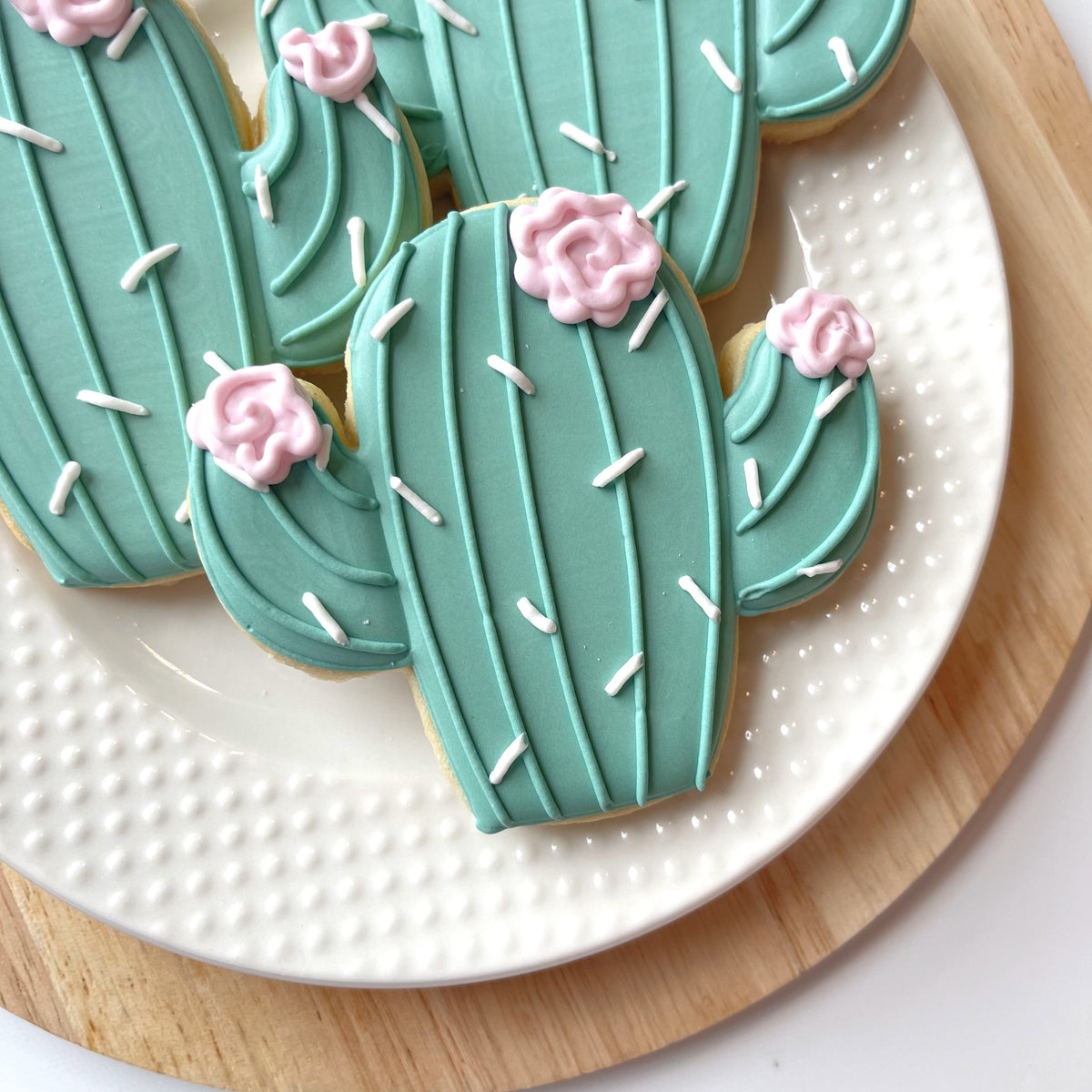 Teal cactus-shaped sugar cookies decorated with pink icing roses and white sprinkles from western decorating online class recording
