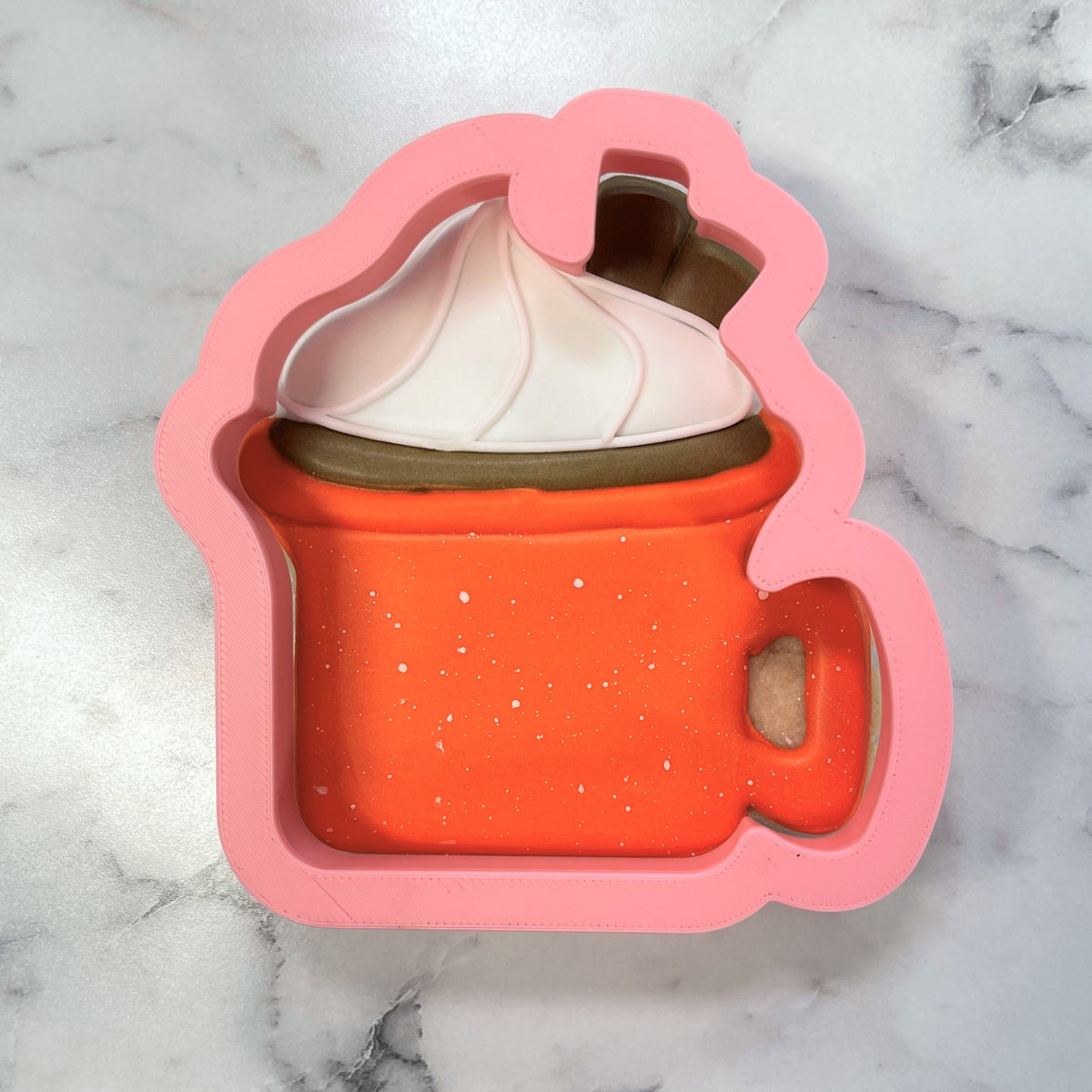 Pink silicone campfire mug cookie cutter shaped like a hot cocoa mug with white whipped cream and chocolate drizzle details
