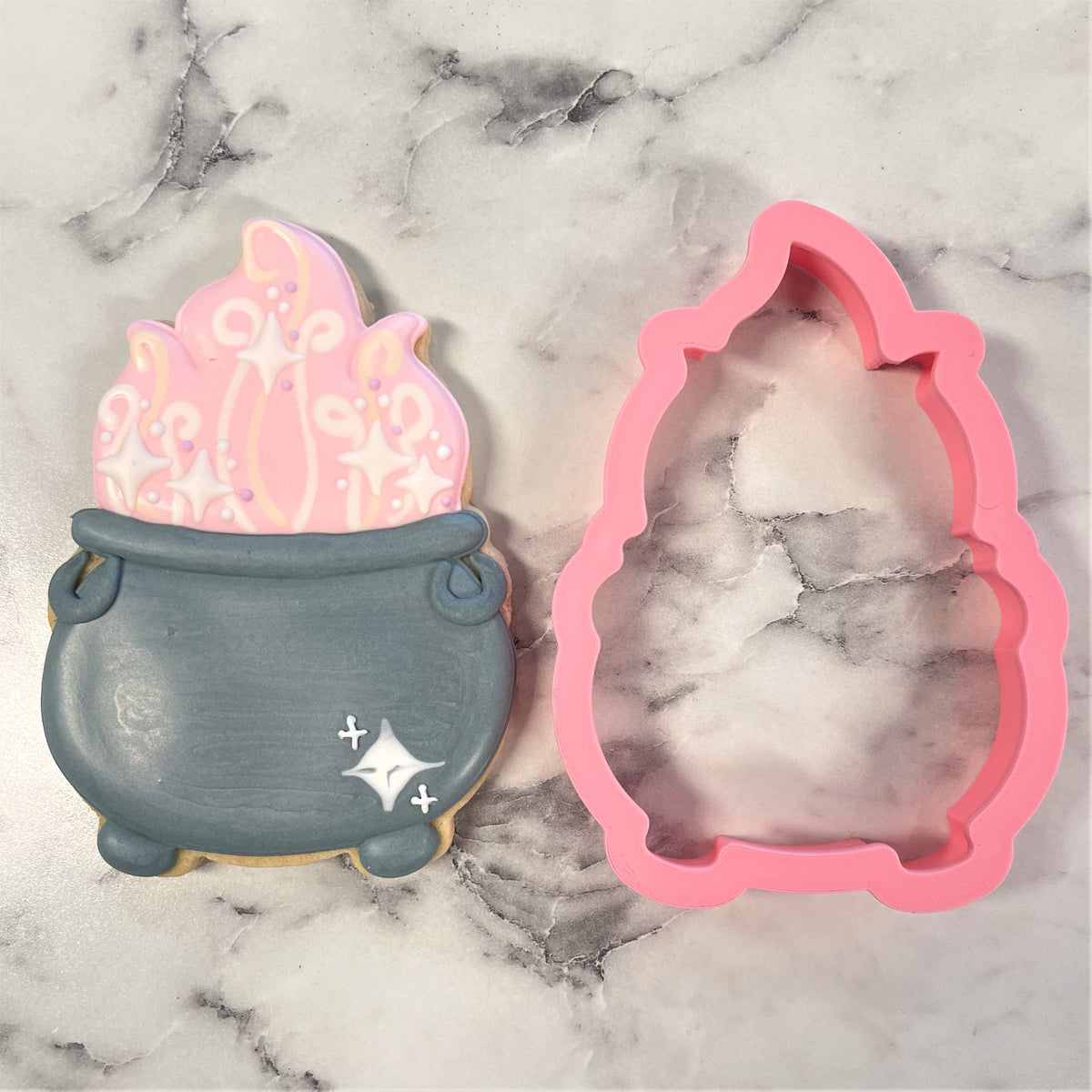 Pink silicone witch cauldron cookie cutter next to decorated sugar cookie shaped like the cauldron