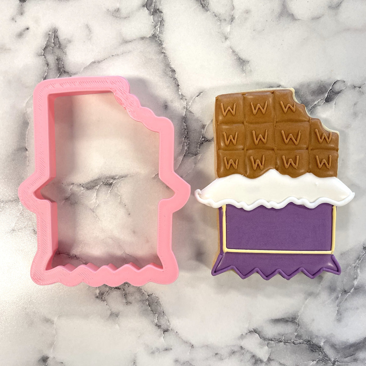Pink plastic chocolate bar cookie cutter with a decorated sugar cookie featuring brown white and purple icing
