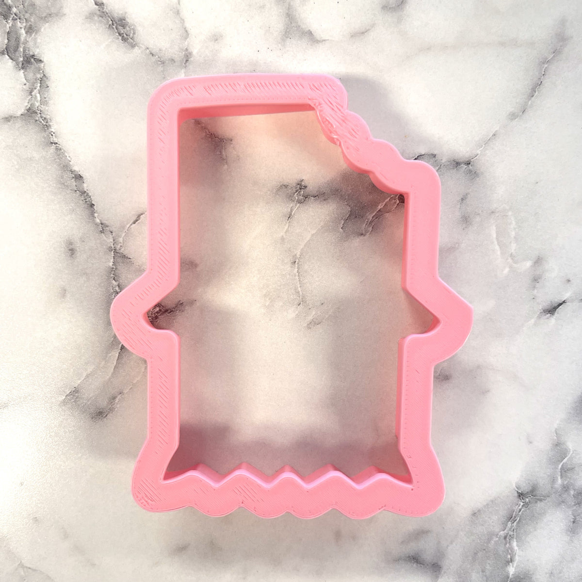 Pink plastic cookie cutter shaped like the state of idaho for chocolate bar cookie cutting and baking use