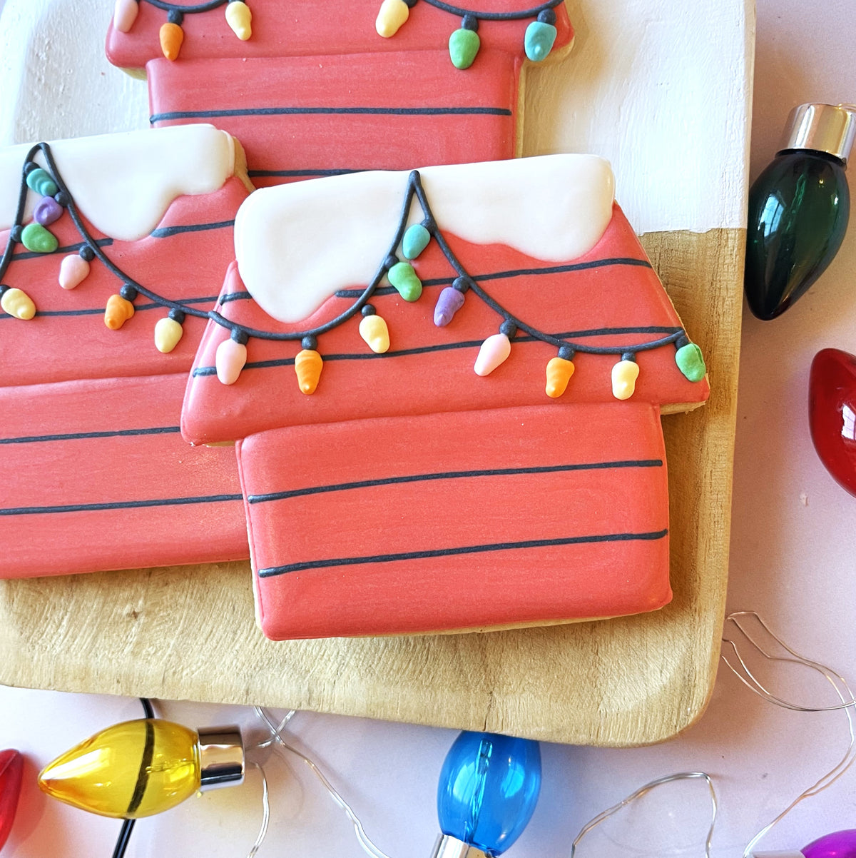 Red sugar cookie shaped like a house with black stripes and white icing snow decorated with colorful candy lights from christmas movie 2.0 cookie cutter bundle