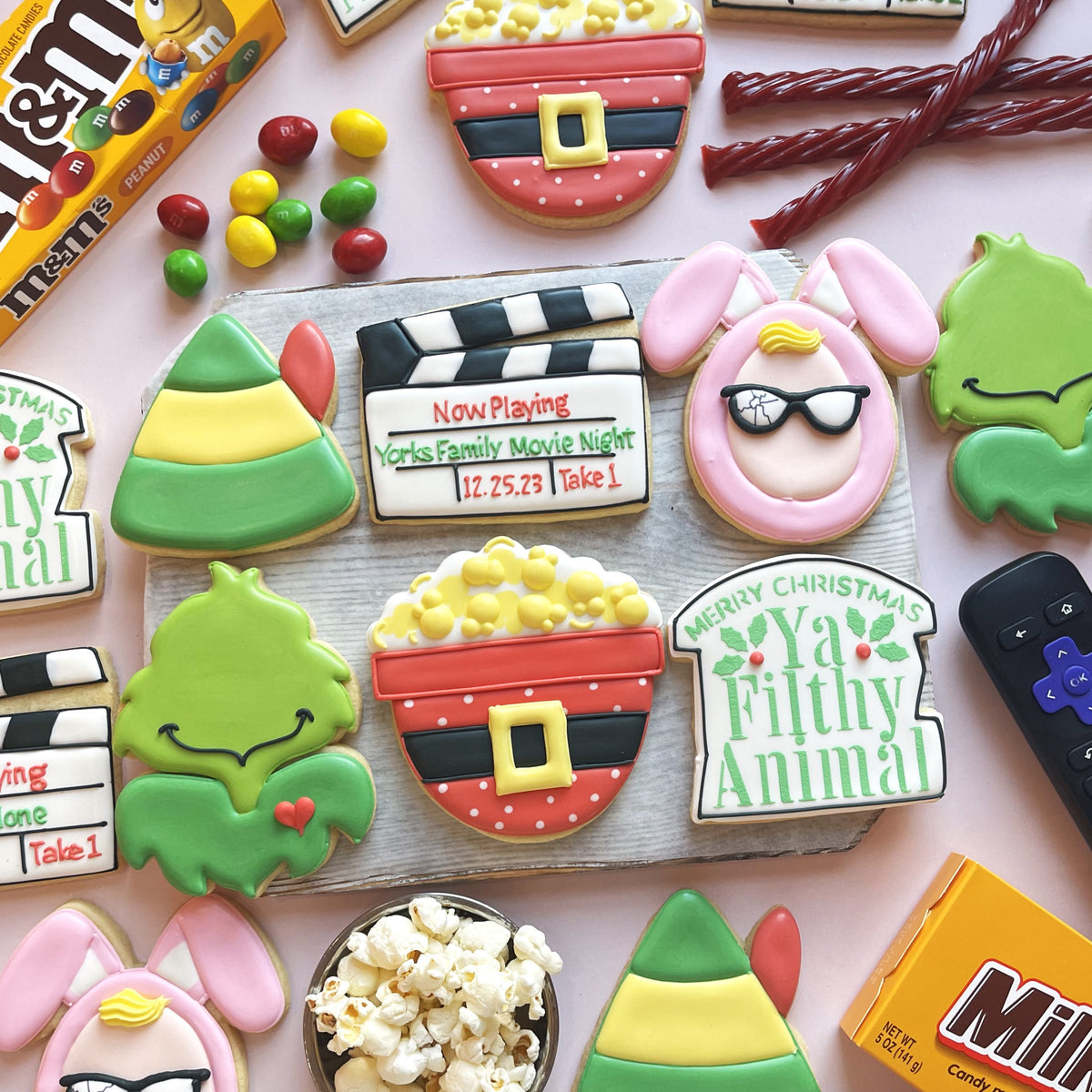 A festive holiday-themed cookie shaped like a popcorn bucket with red and black stripes and a yellow buckle made using a clapperboard cookie cutter