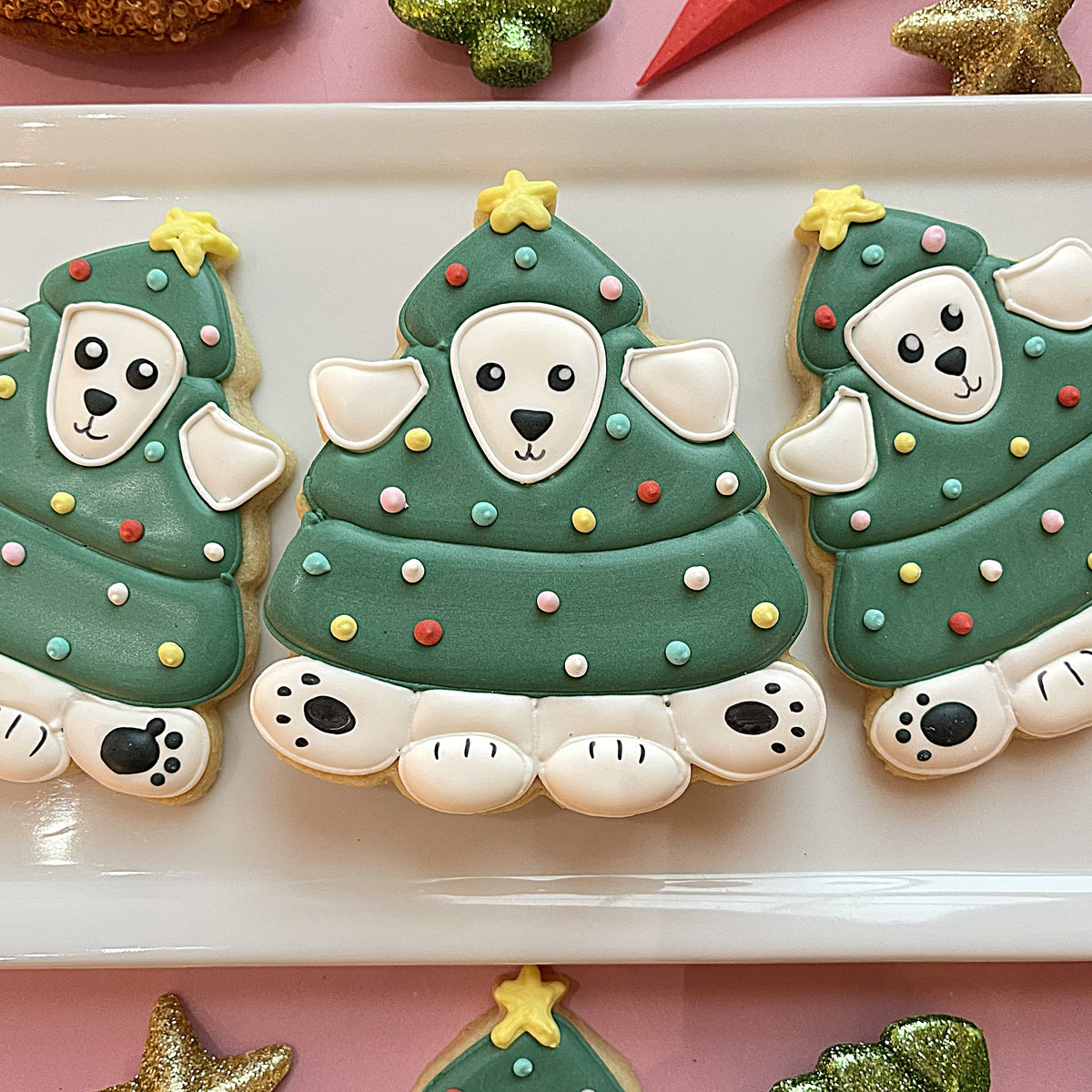 Green frosted christmas tree-shaped cookies with white dog faces and colorful candy decorations made using a christmas tree pup cookie cutter
