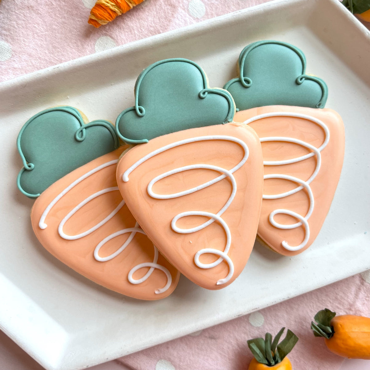 Pastel peach and teal carrot shaped sugar cookies with white icing made using bunny farmer cookie cutter bundle with stencil
