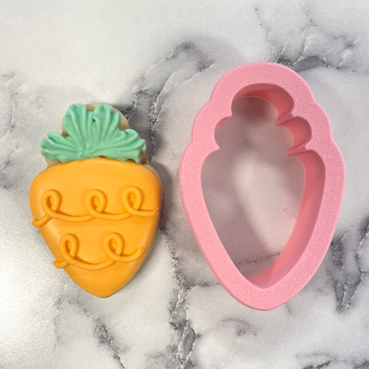 Chunky carrot cookie cutter with a vibrant orange carrot-shaped cookie and matching pink silicone baking mold
