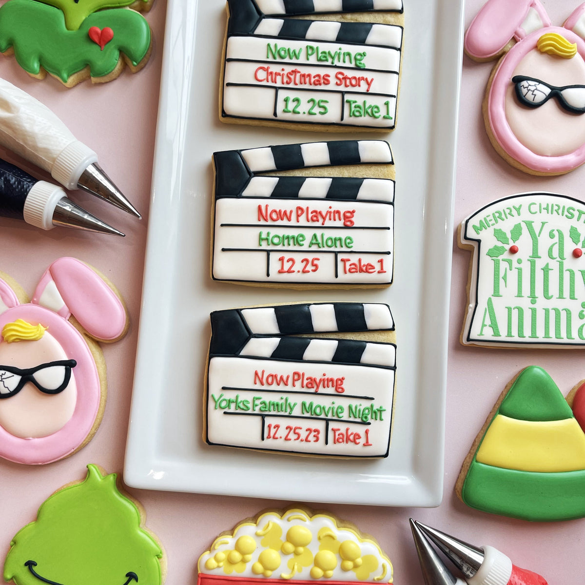 White sugar cookies shaped like clapperboards decorated with black and white stripes and colorful film titles using clapperboard cookie cutter