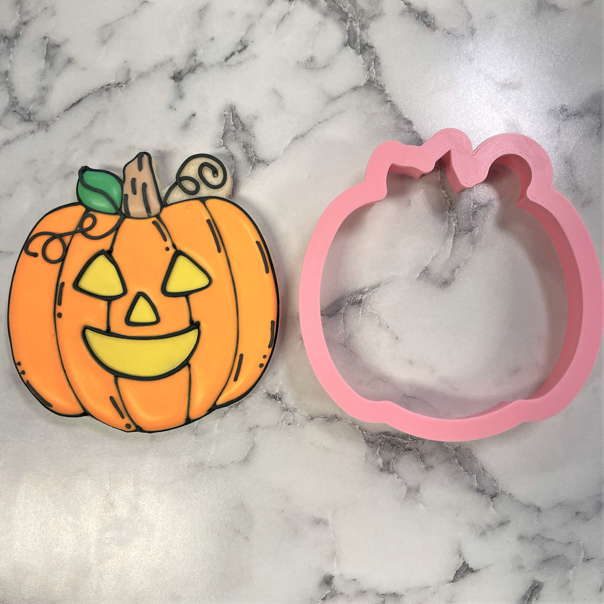 Comic jack-o-lantern cookie cutter in orange and yellow with green stem and pink silicone mold for baking