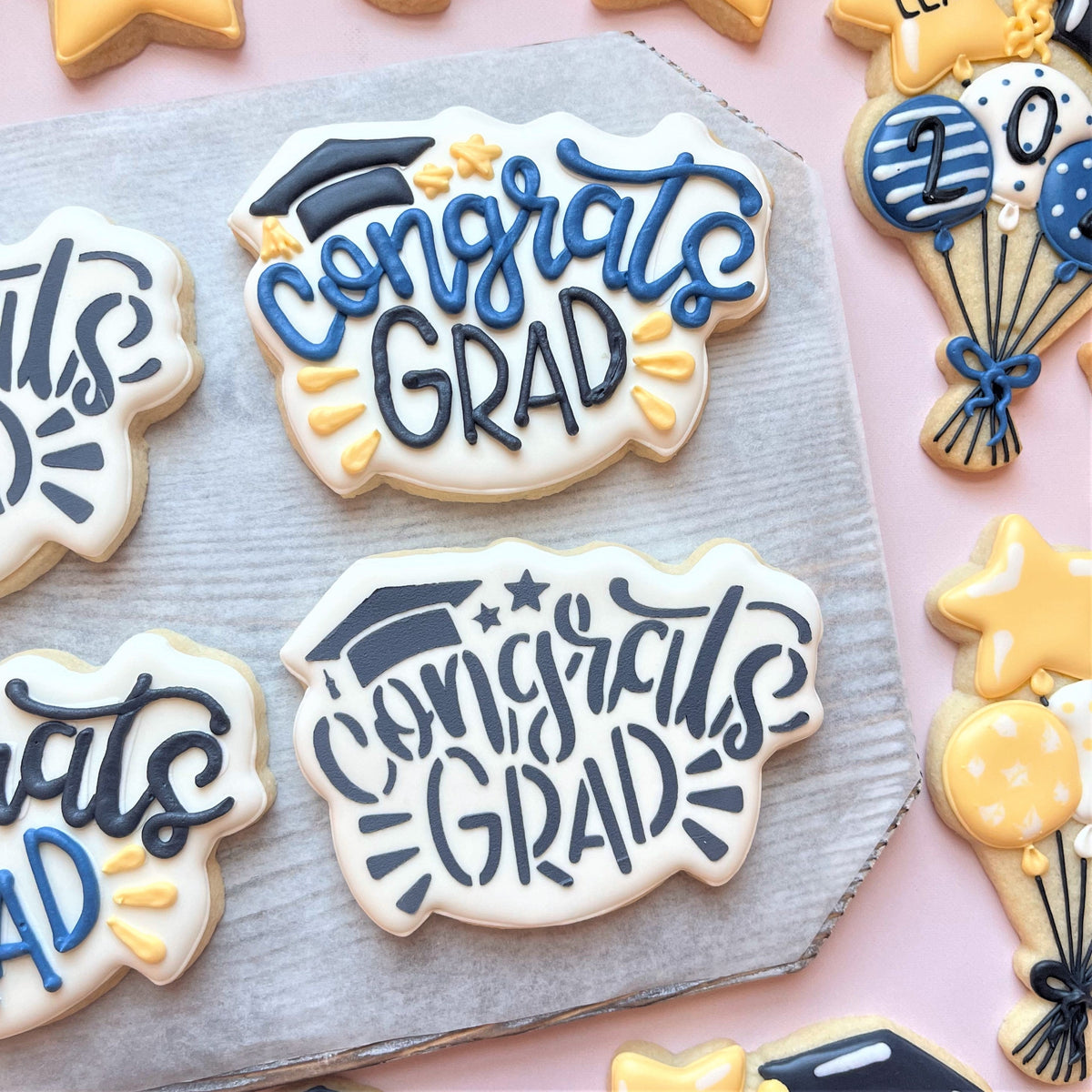 White frosted cookie shaped like a graduation cap with blue and black icing reading congrats grad for grad online decorating class recording