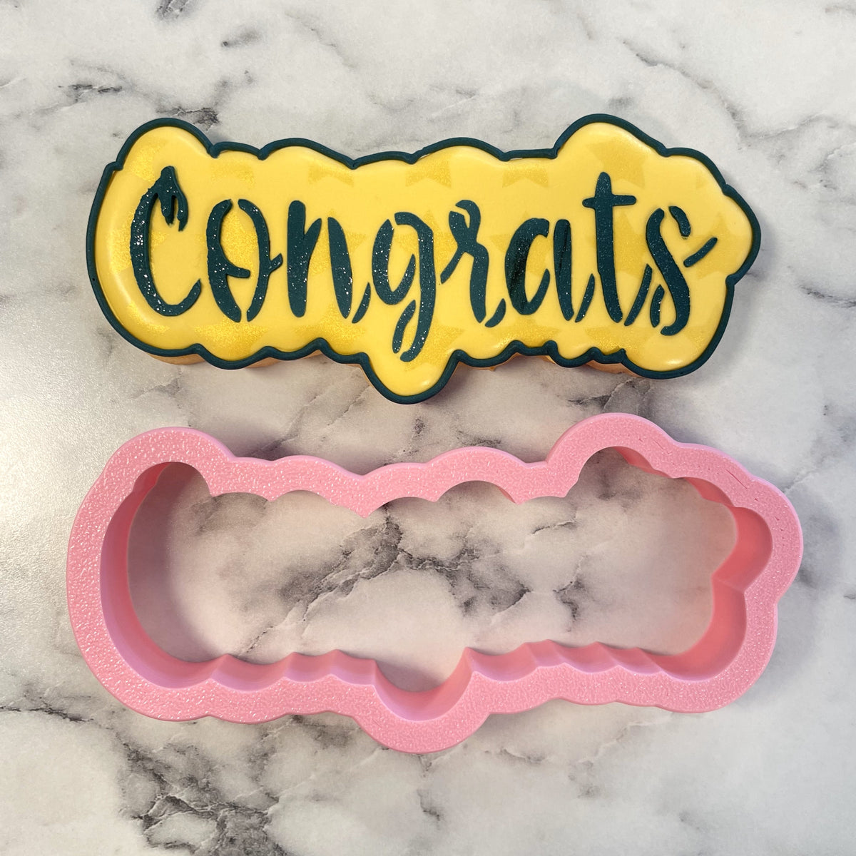 Yellow and black glittery congrats cookie cutter with pink silicone mold for baking and decorating cookies