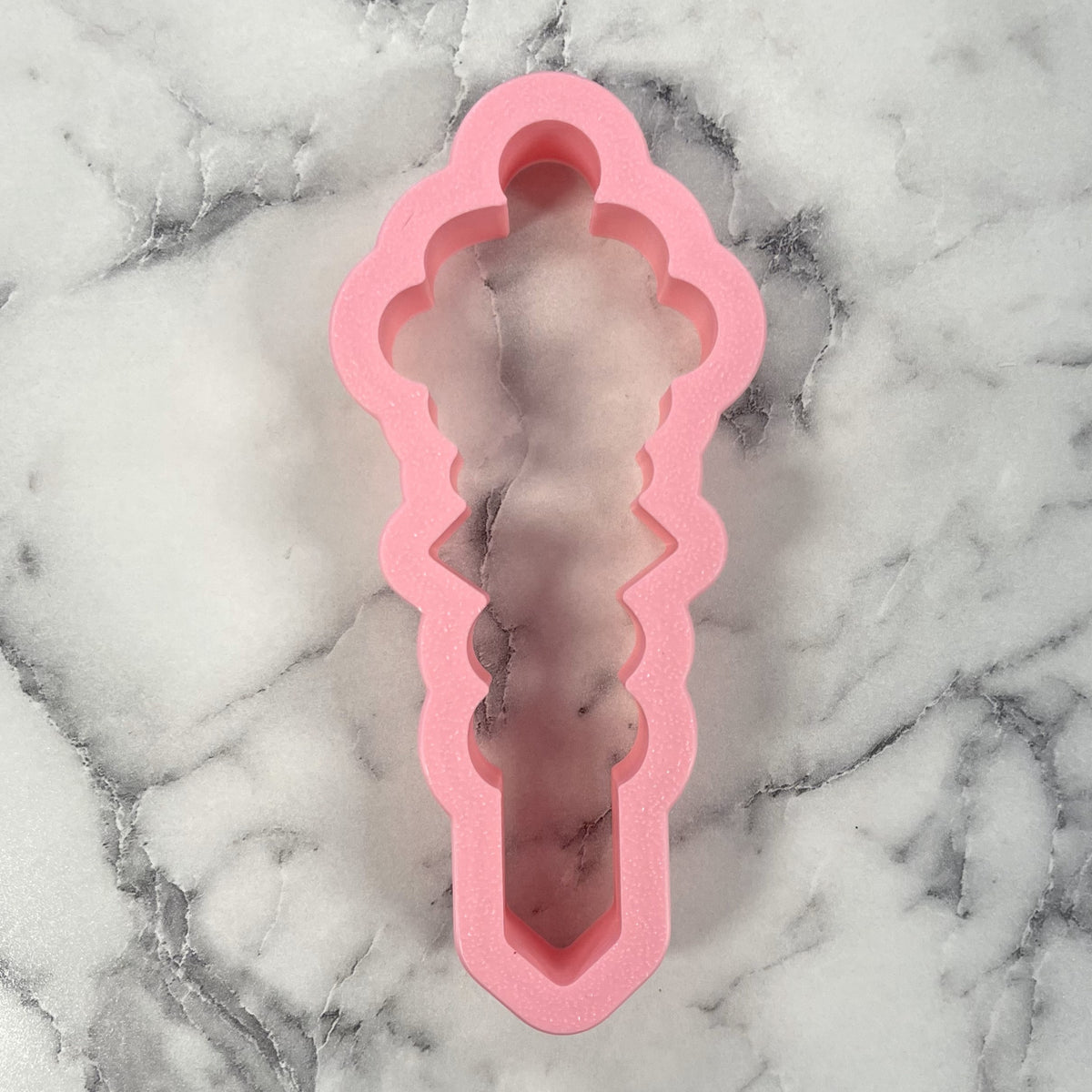 Pink silicone cookie scribe cookie cutter shaped like a sword with scalloped edges and an ornate handle design