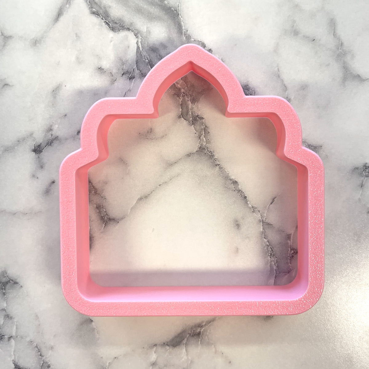 Pink silicone cookie cutter shaped like a house with an arched top for cozy jar candle baking and crafts