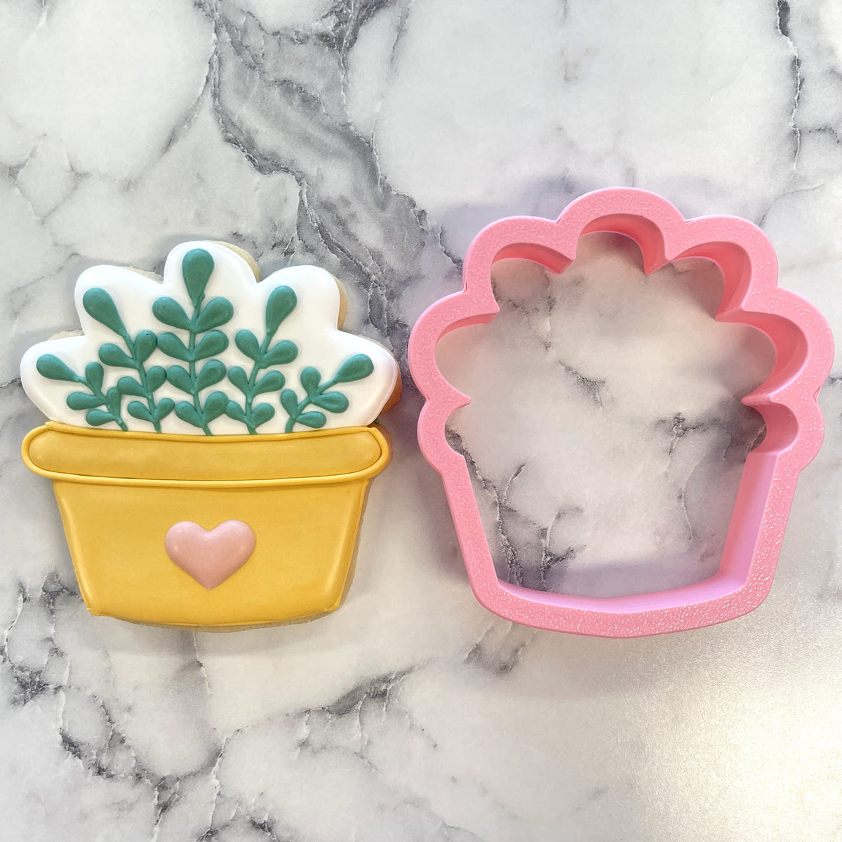 Cozy house plant cookie cutter with yellow potted plant cookie green icing leaves pink heart and matching pink silicone mold