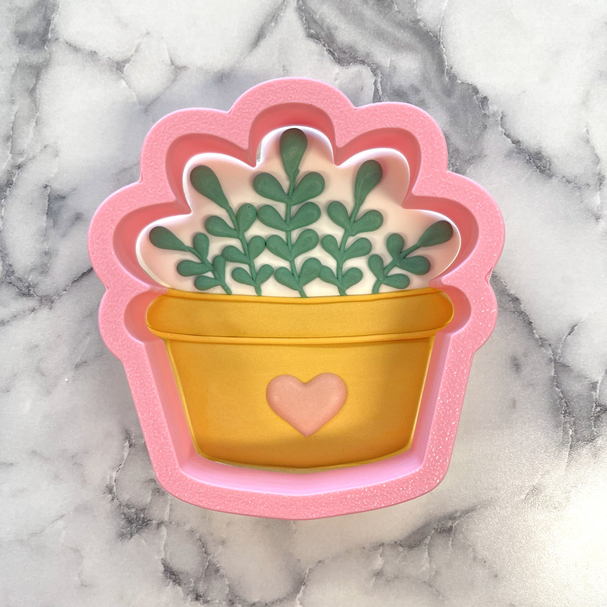 Cozy house plant cookie cutter made of pink and yellow silicone shaped like a potted plant with green leaves