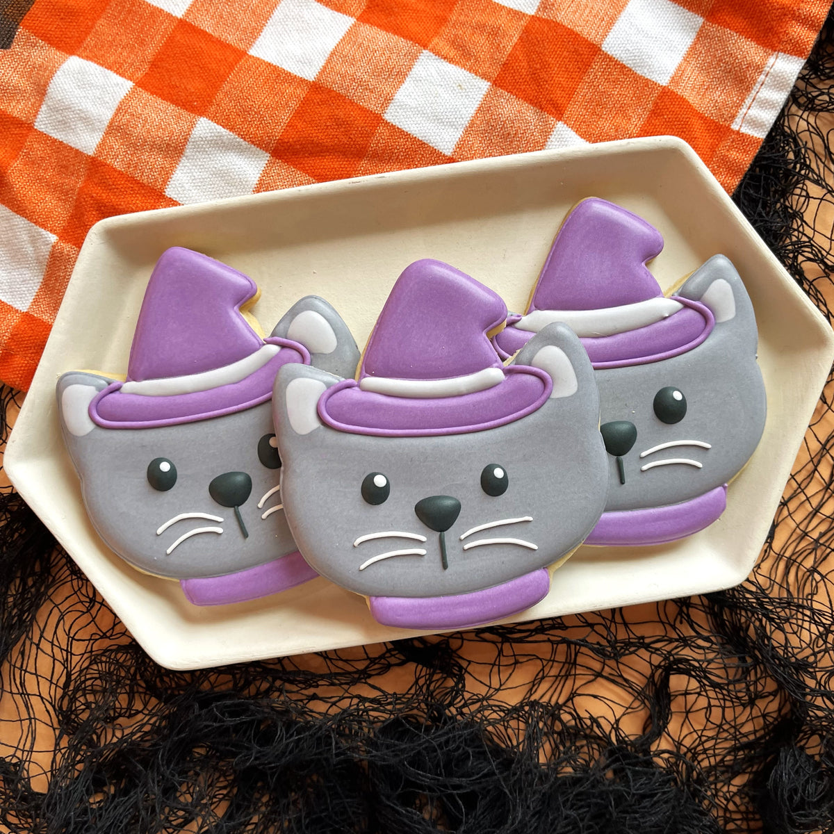 Three gray cat-shaped cookies with purple witch hats and white icing made using cute chubby halloween cookie cutter bundle