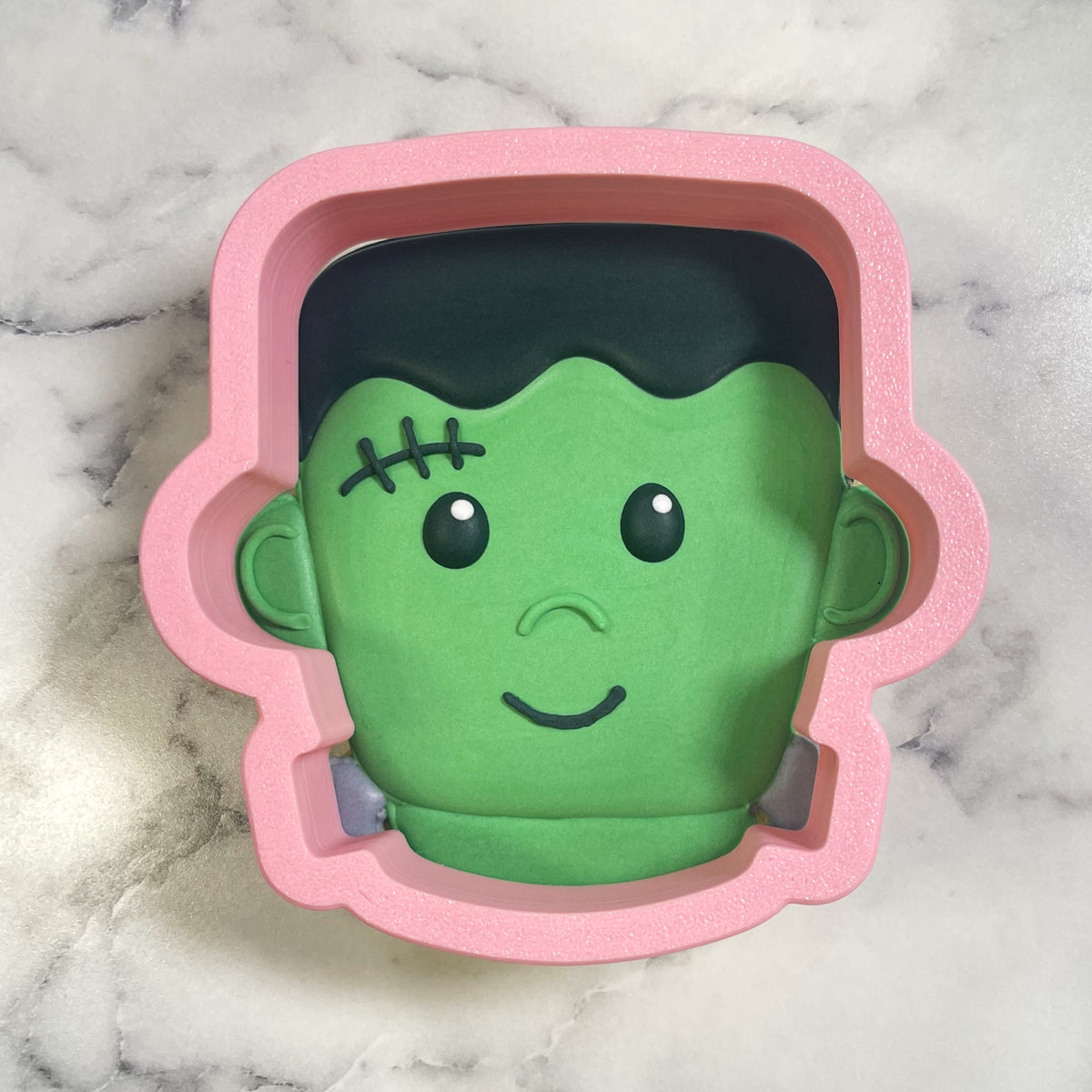 Pink silicone cute chubby frank cookie cutter shaped like cartoon frankensteins head with green face and stitched details