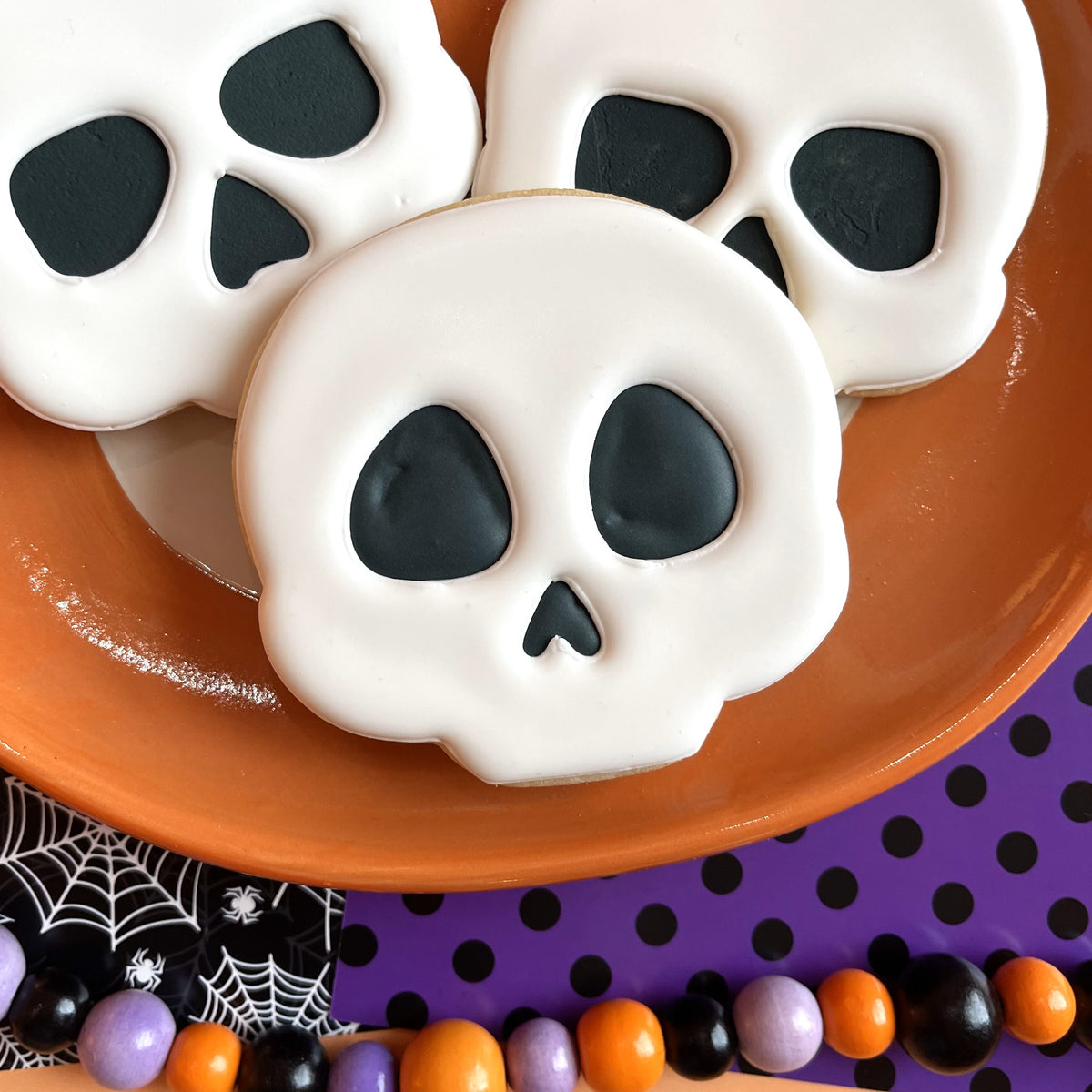Cute chubby halloween cookie cutter bundle white frosted skull shaped cookies with black icing on orange plate