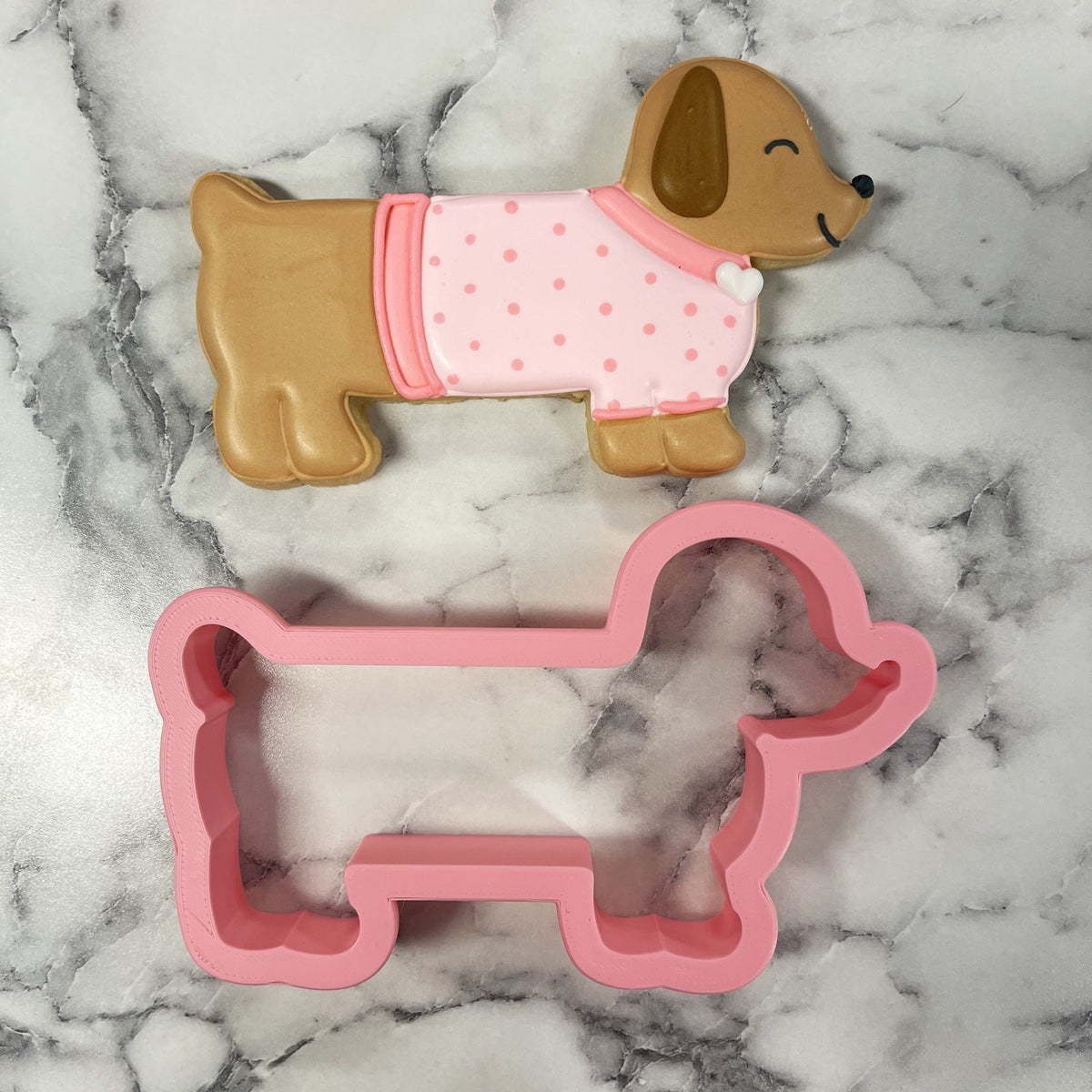 Pink plastic dachshund cookie cutter with matching pink polka-dot dog-shaped cookie for baking fun