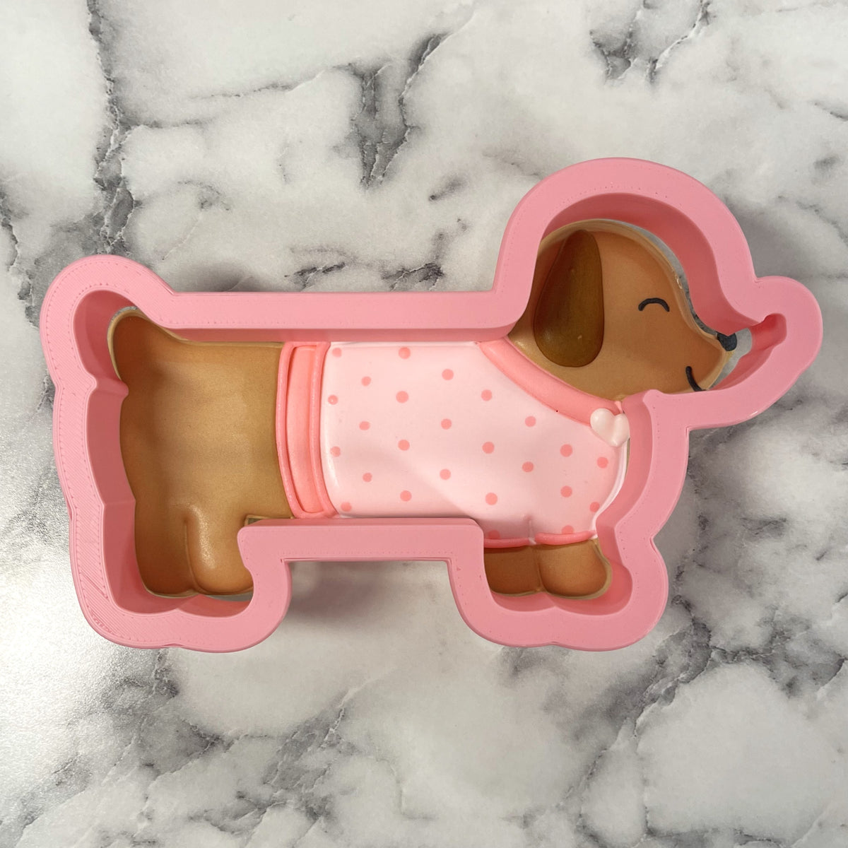 Pink silicone dachshund cookie cutter mold shaped like a brown puppy in pink polka-dot pajamas for baking