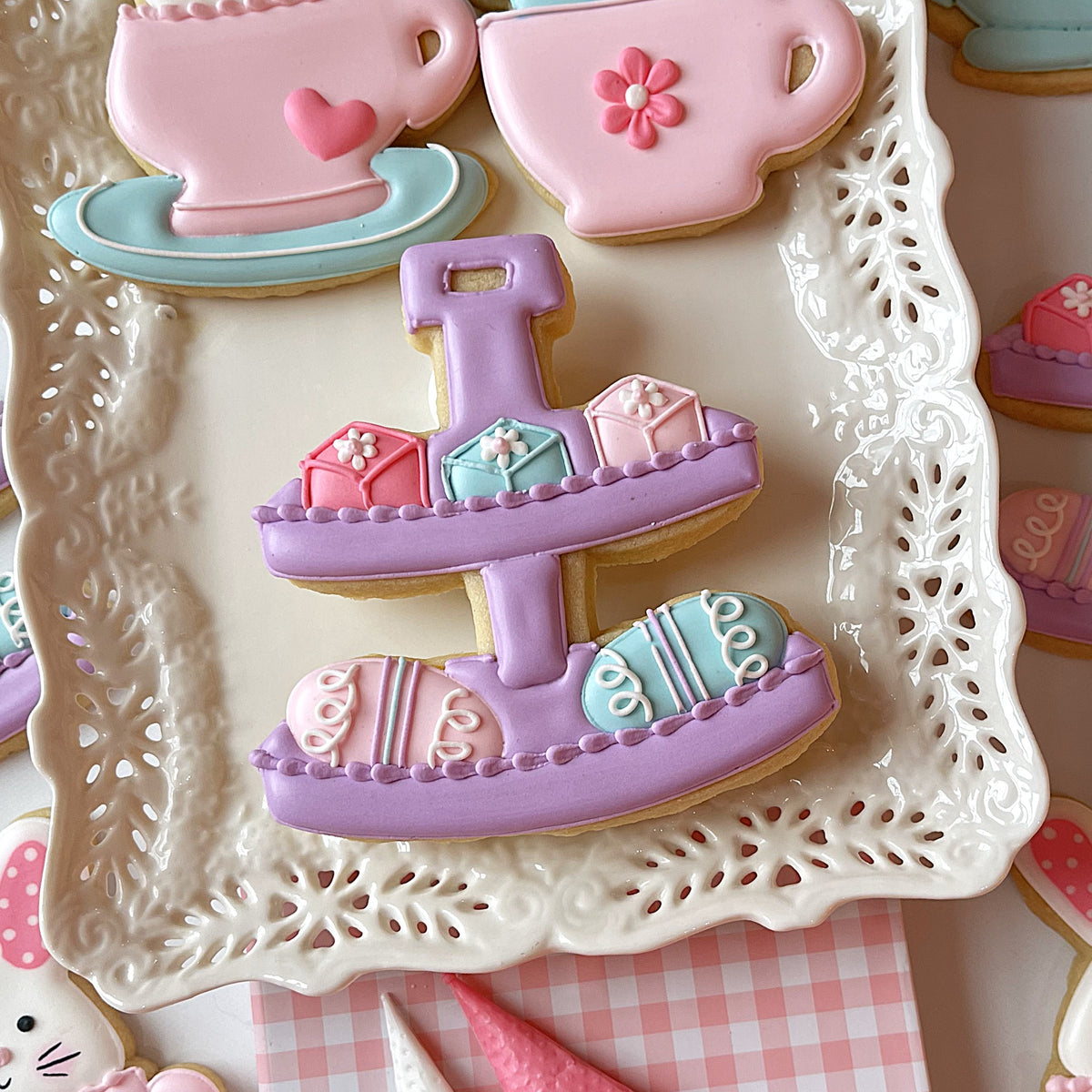 Pastel purple two-tiered cookie stand with delicate icing and pastel-colored boxes for easter 2025 cookie cutter set