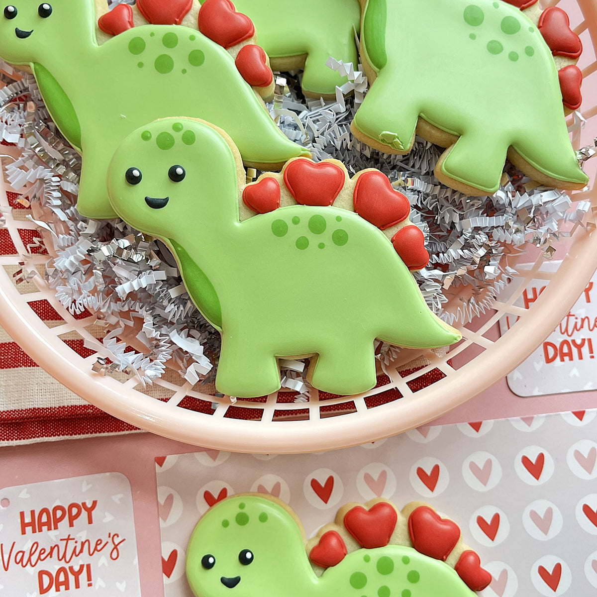 Green dinosaur shaped cookies with red heart spikes and black dot eyes decorated in icing from valentine 2025 cookie cutter set