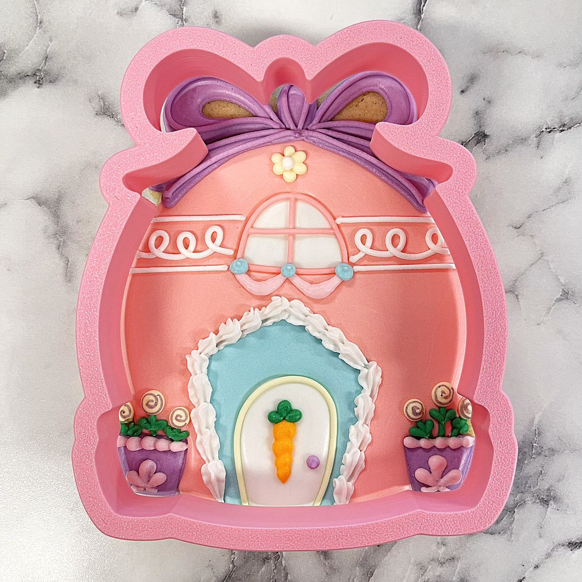 Pink silicone easter egg house cookie cutter shaped like a whimsical house with purple bow and decorative plants