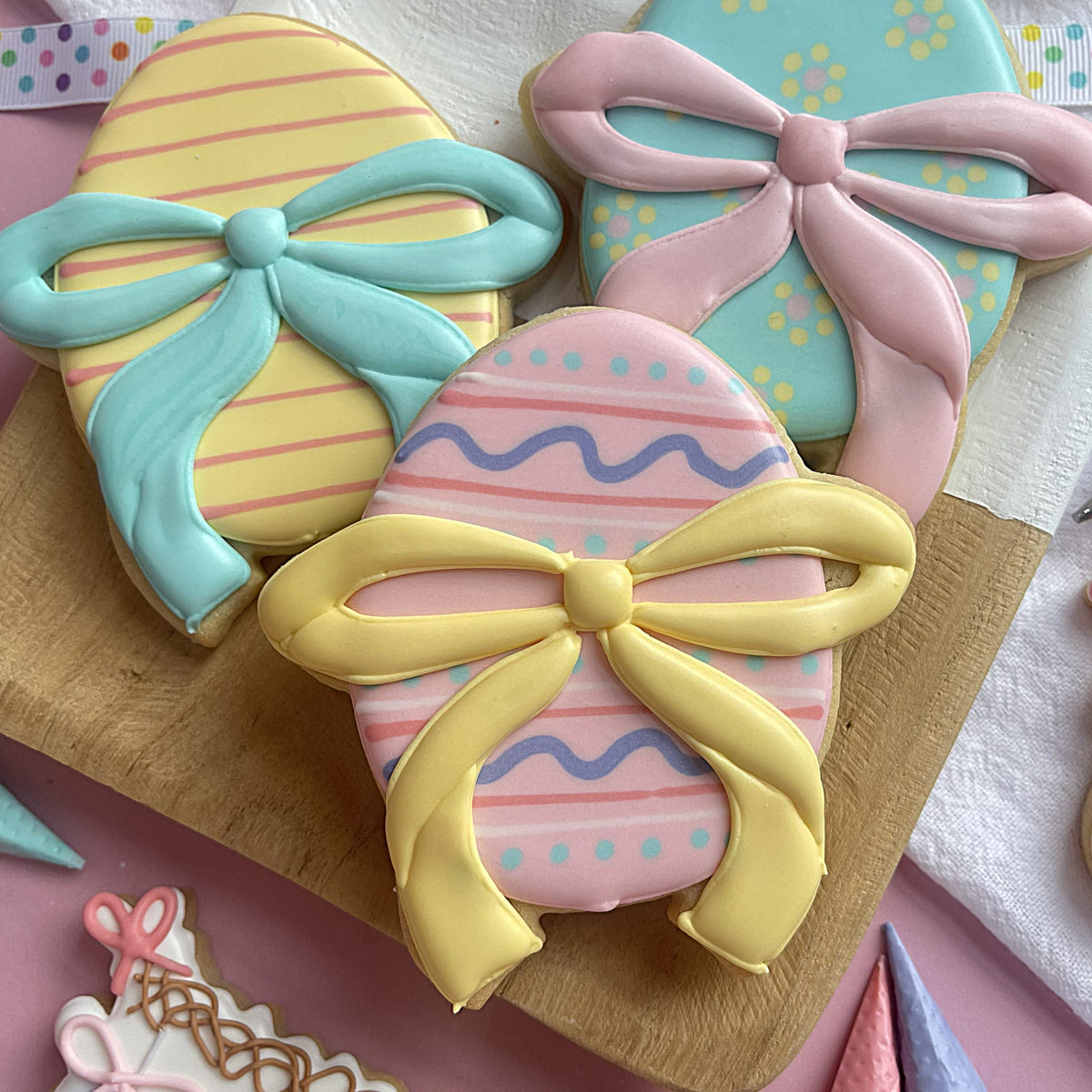 Pastel-colored easter egg-shaped cookies decorated with icing bows and stripes made using egg with ribbon cookie cutter