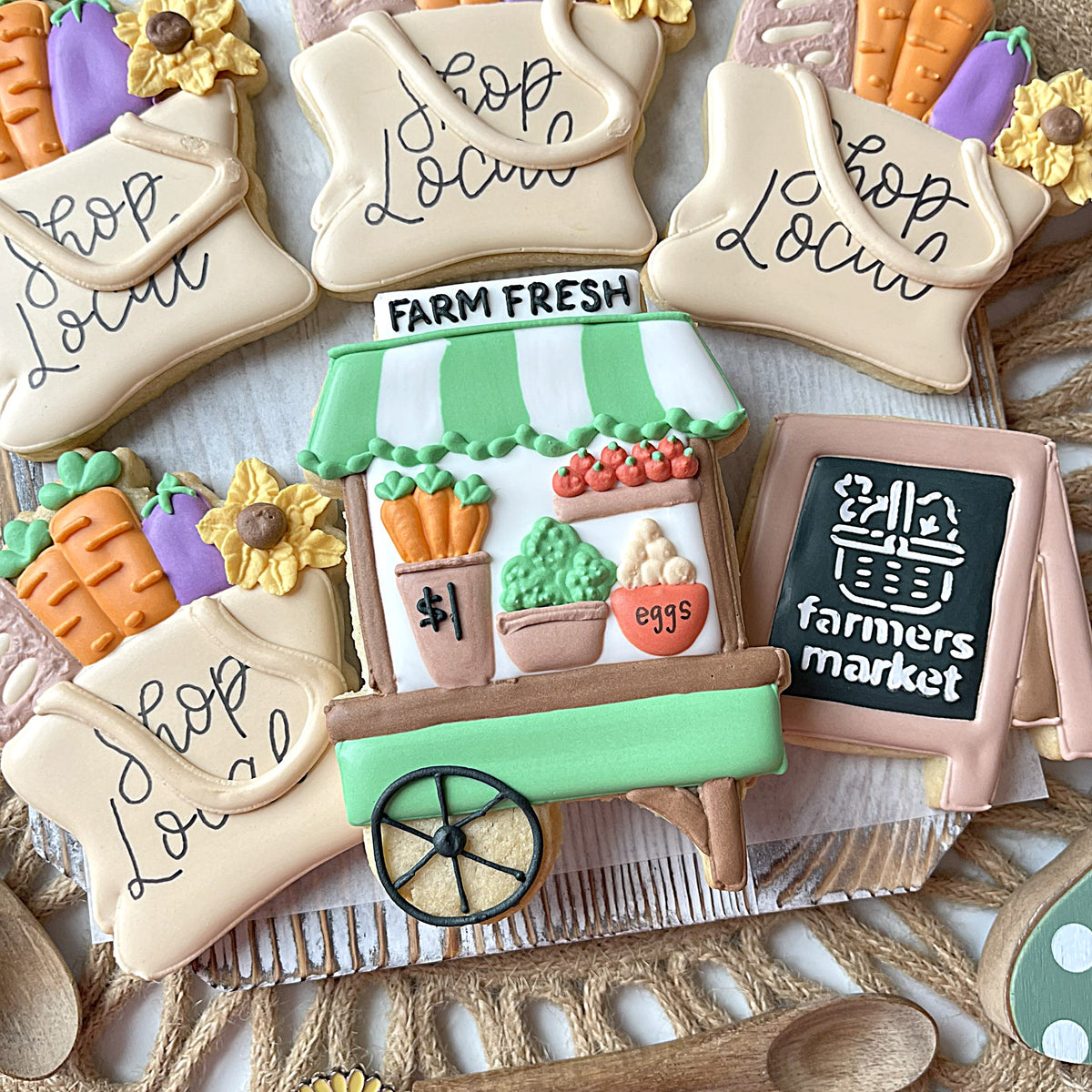 A green and white striped cookie shaped like a farmers market cart decorated with fondant vegetables and chalkboard sign made with market tote flour box club cookie cutter
