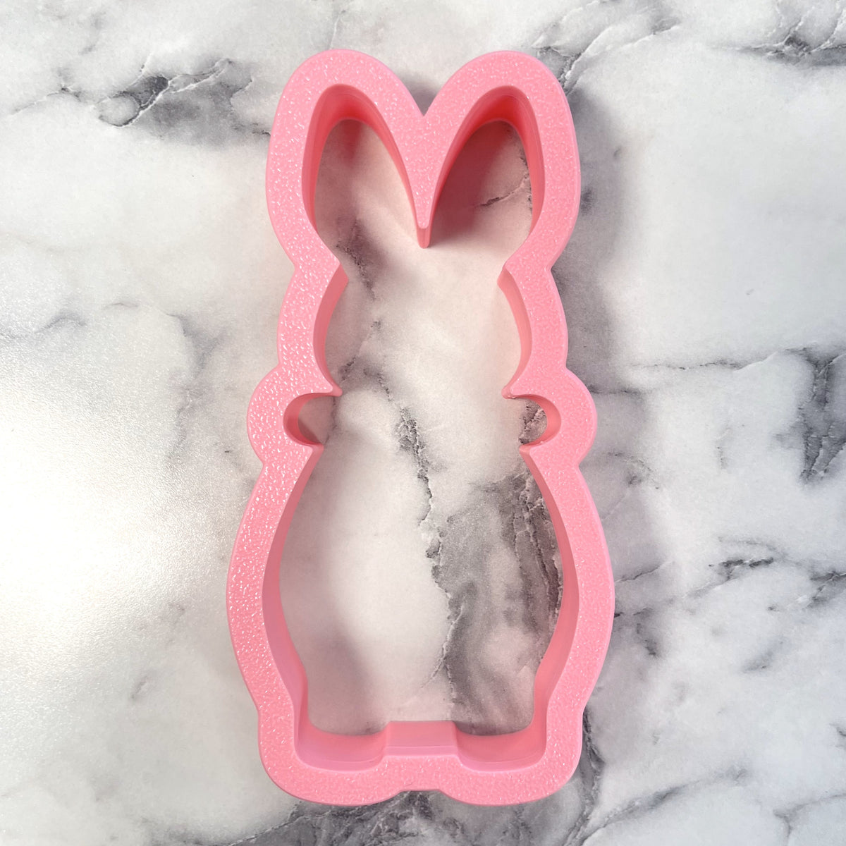 Pink bunny shaped silicone mold filled with marbled white and gray substance for flocked bunny with bow cookie cutter