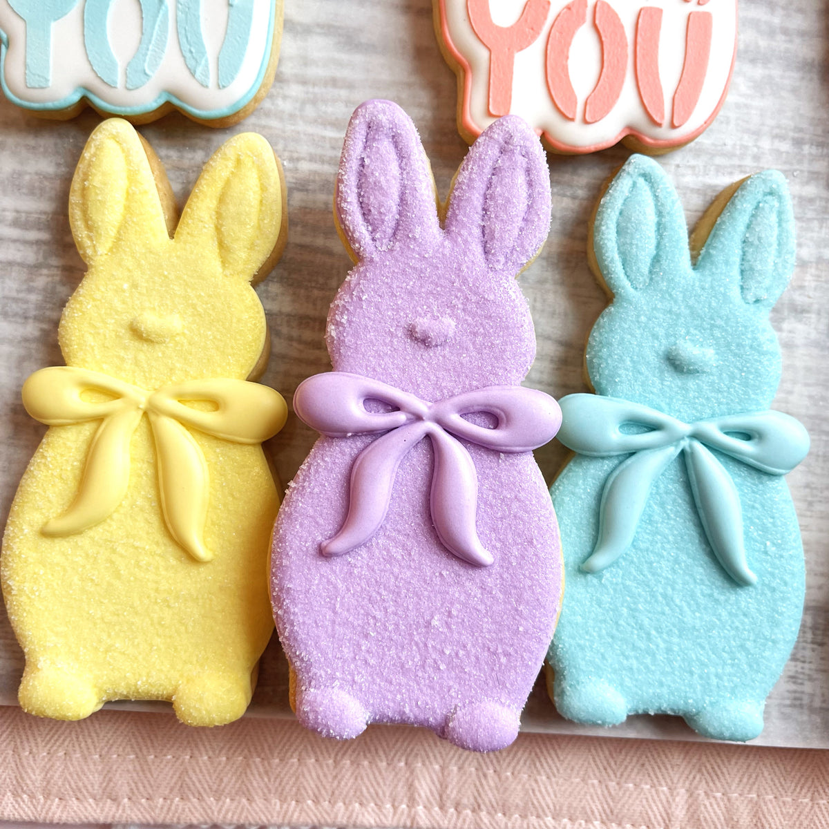 Pastel-colored sugar-coated bunny cookies with decorative bows made using a flocked bunny with bow cookie cutter