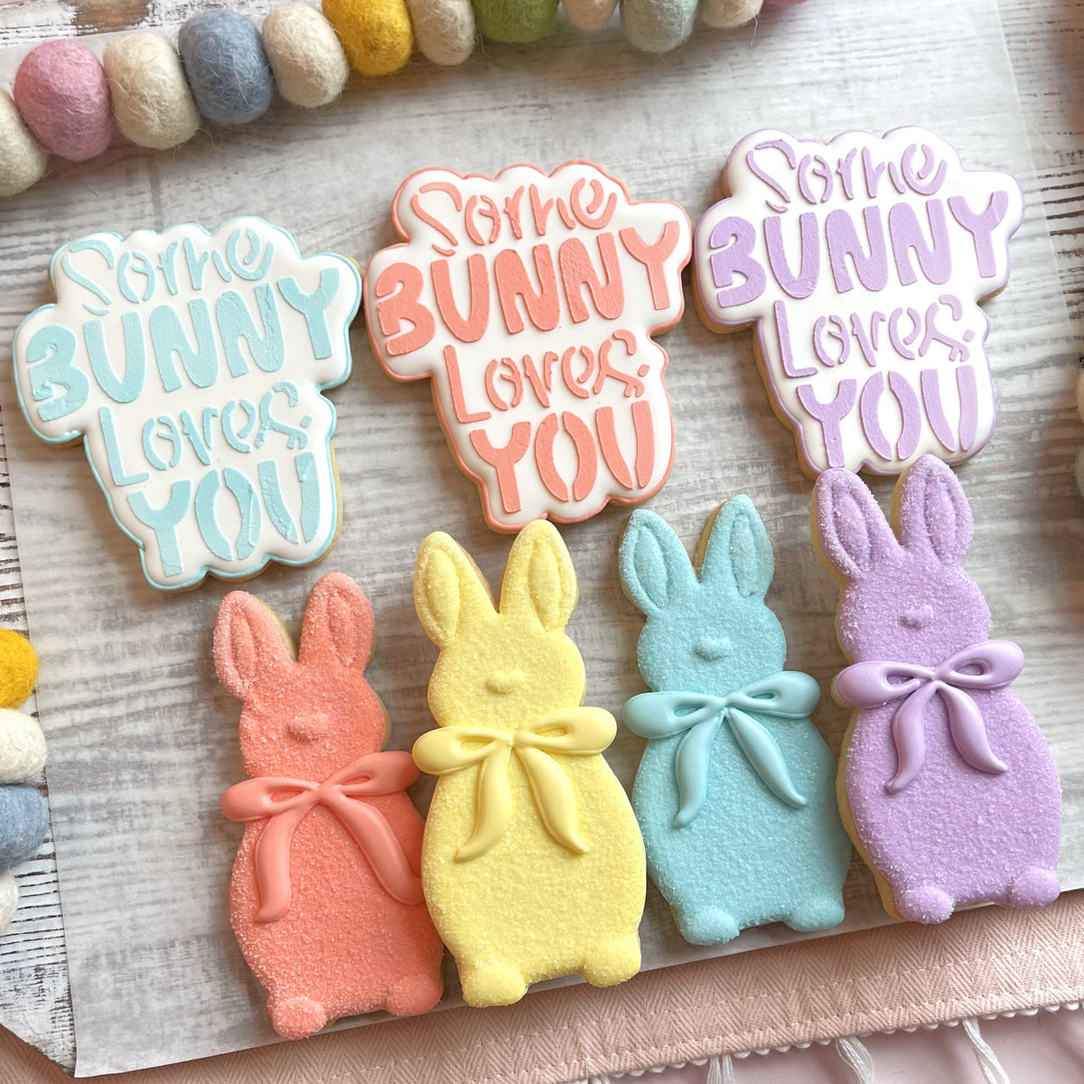 Pastel-colored bunny-shaped sugar cookies decorated with icing bows made using some bunny loves you cookie cutter with stencil bundle