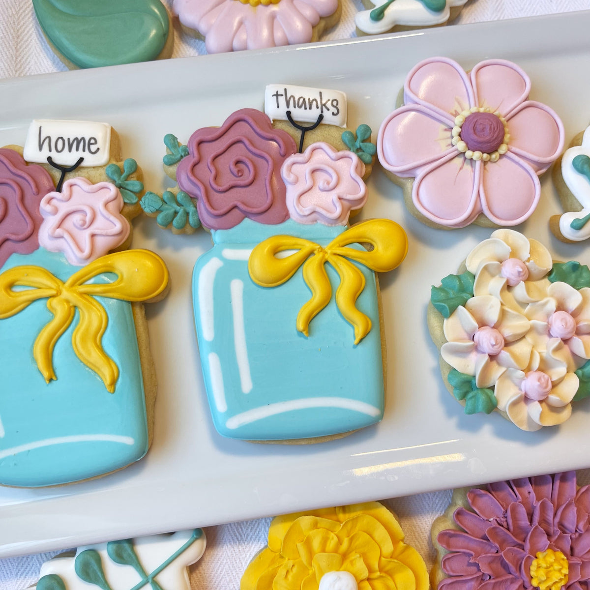 A light blue frosted cookie shaped like a mason jar with yellow ribbon bow and floral decorations from flour box club